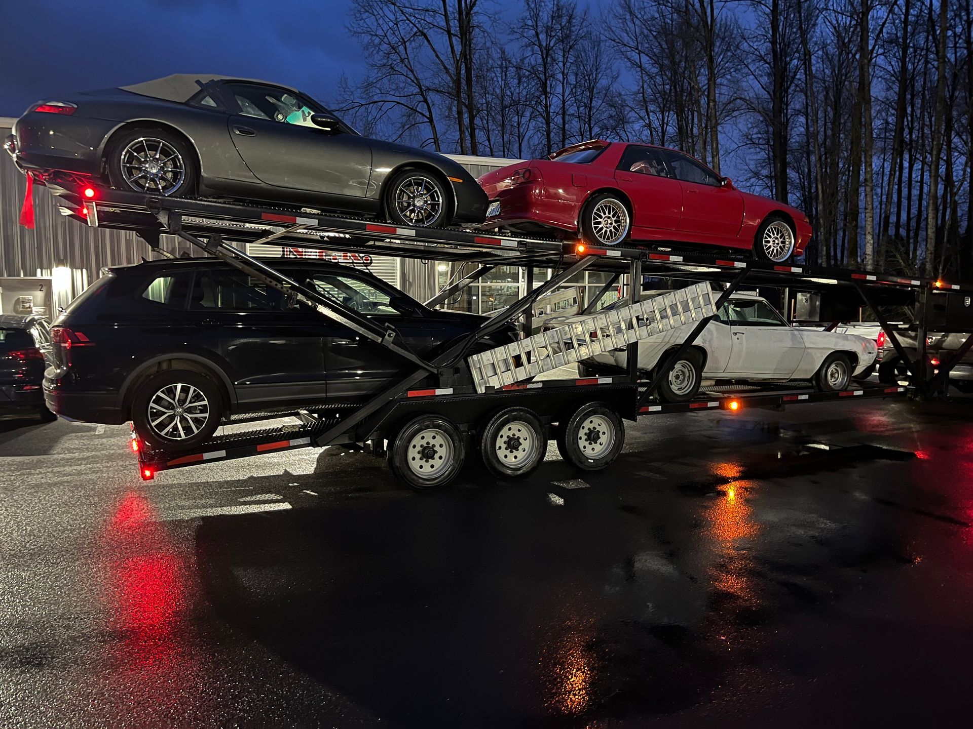 A trailer with three cars on it is parked in a parking lot.