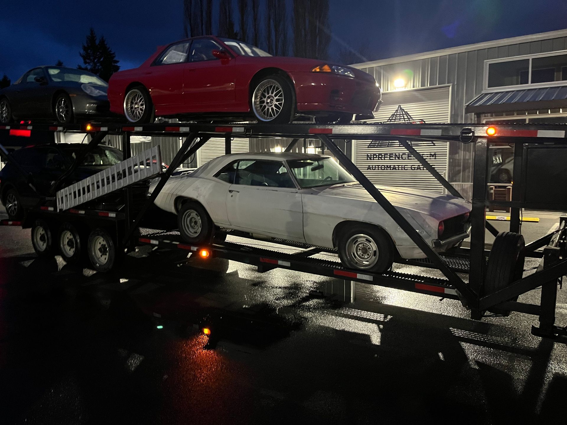 A red car is sitting on top of a white car on a trailer.