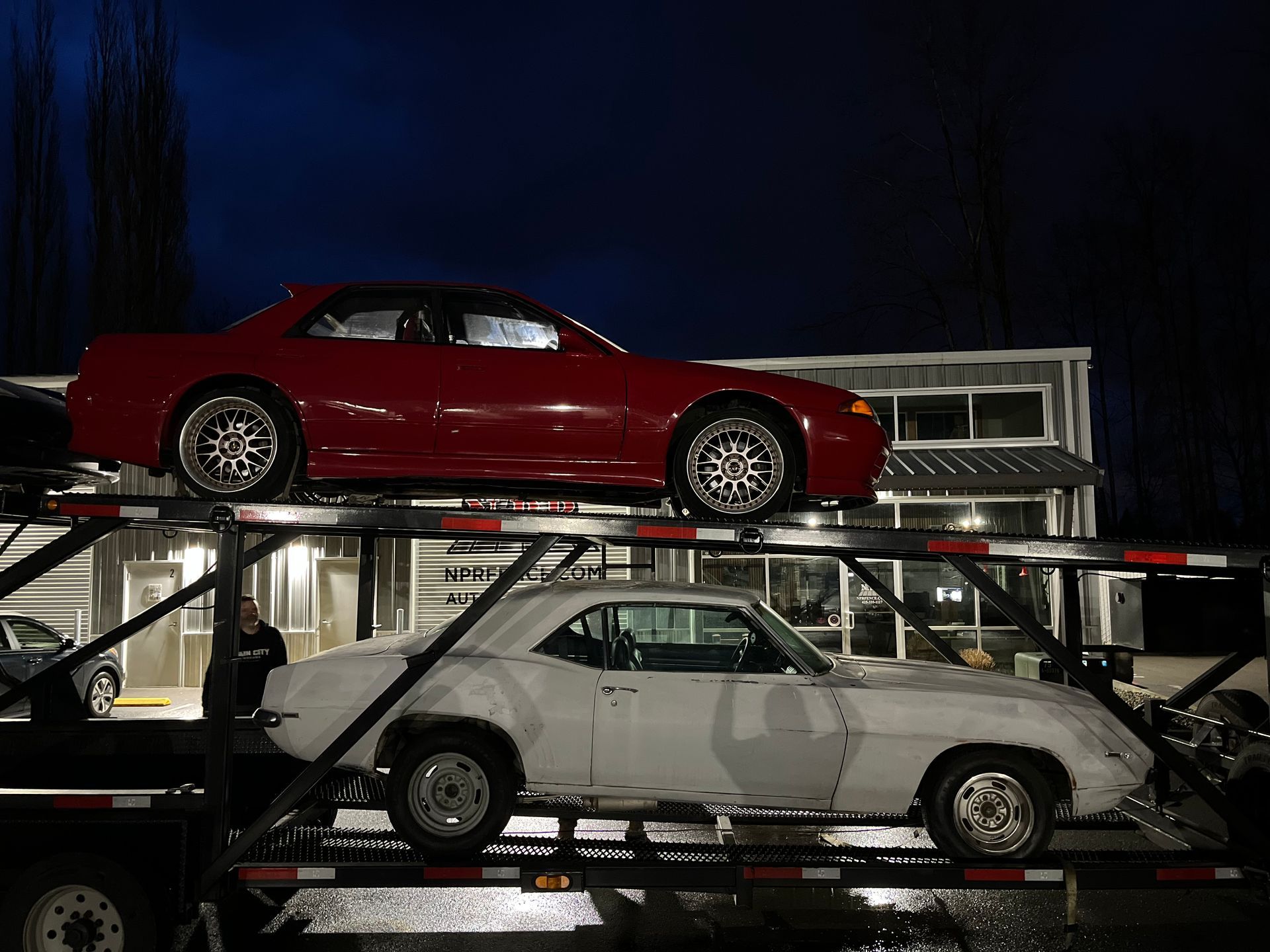 A red car is sitting on top of a white car on a trailer.