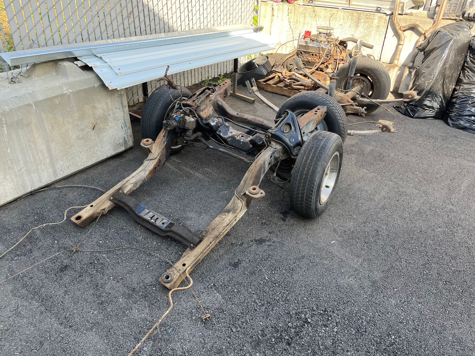 A car frame is laying on the ground next to a fence.