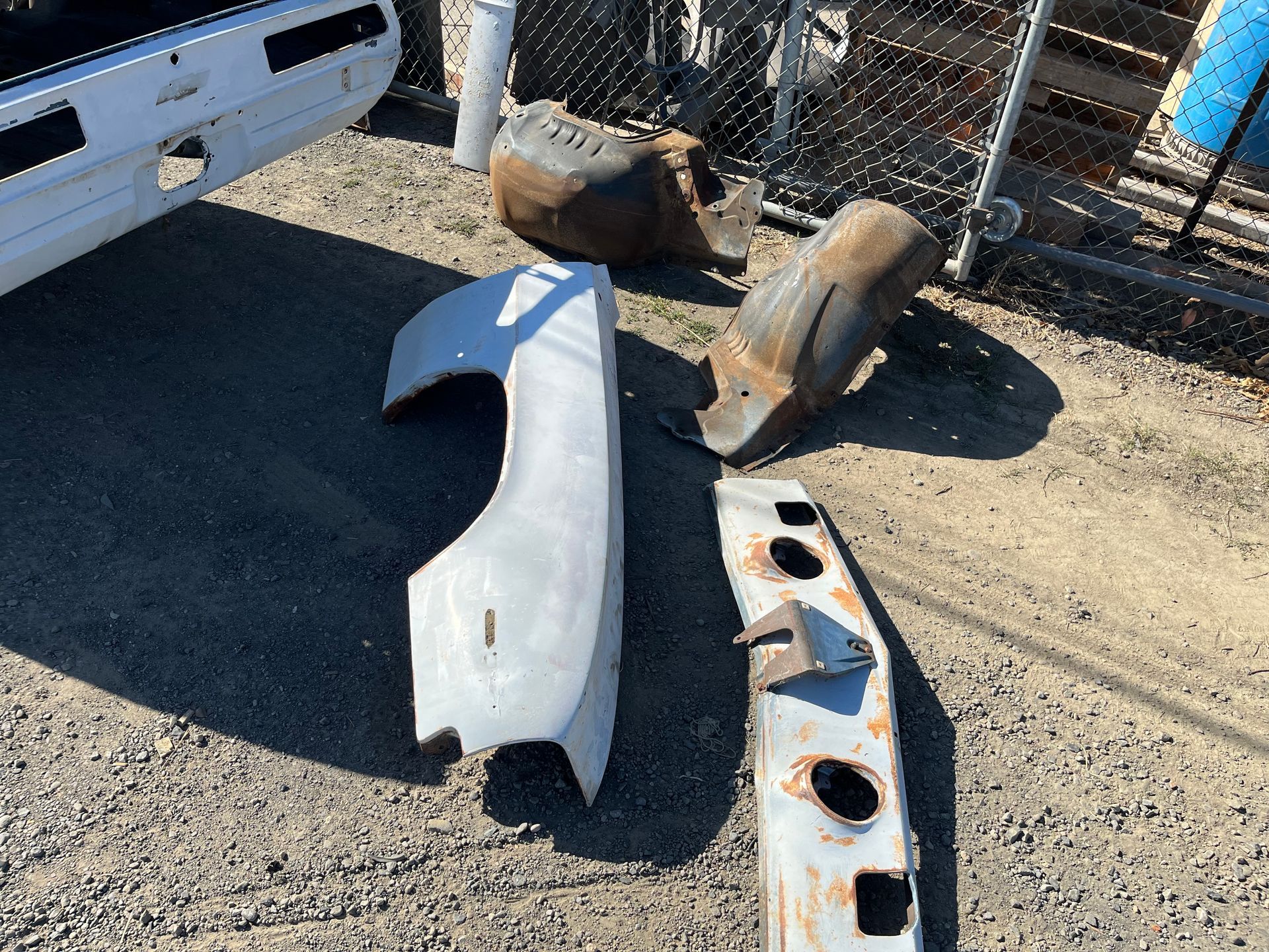 A bunch of car parts are laying on the ground in front of a chain link fence.