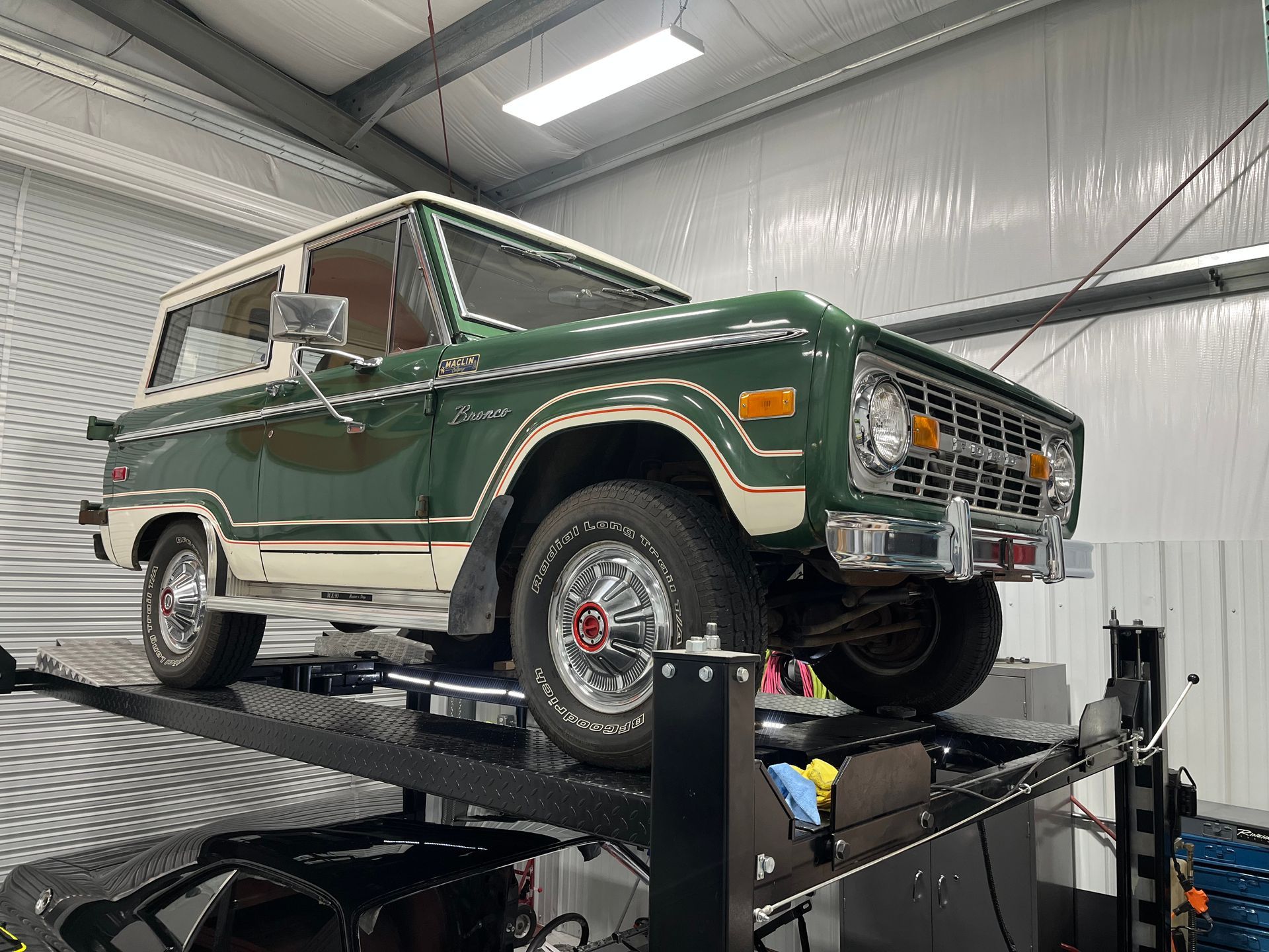 A green and white ford bronco is parked on a lift in a garage.