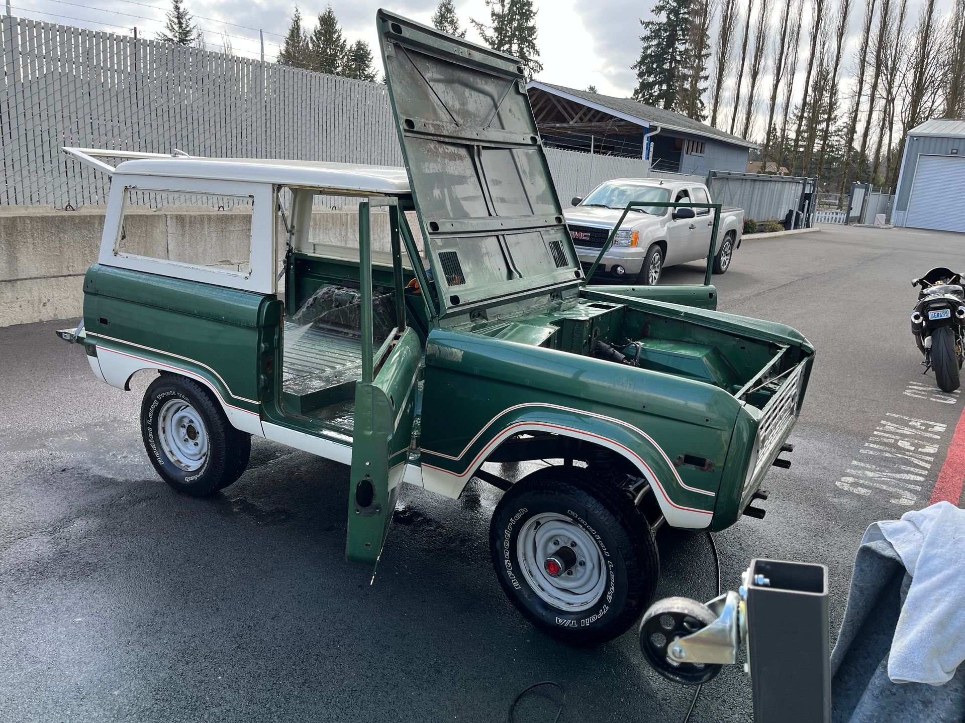 A green and white jeep with the hood up is parked in a parking lot.