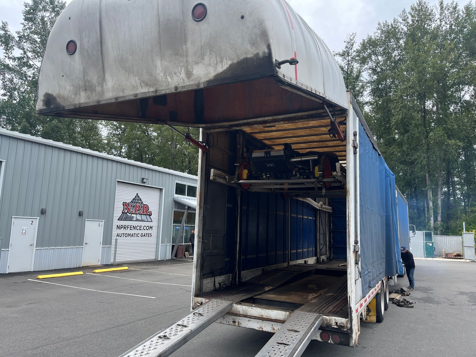 A trailer with the roof open is parked in front of a building.