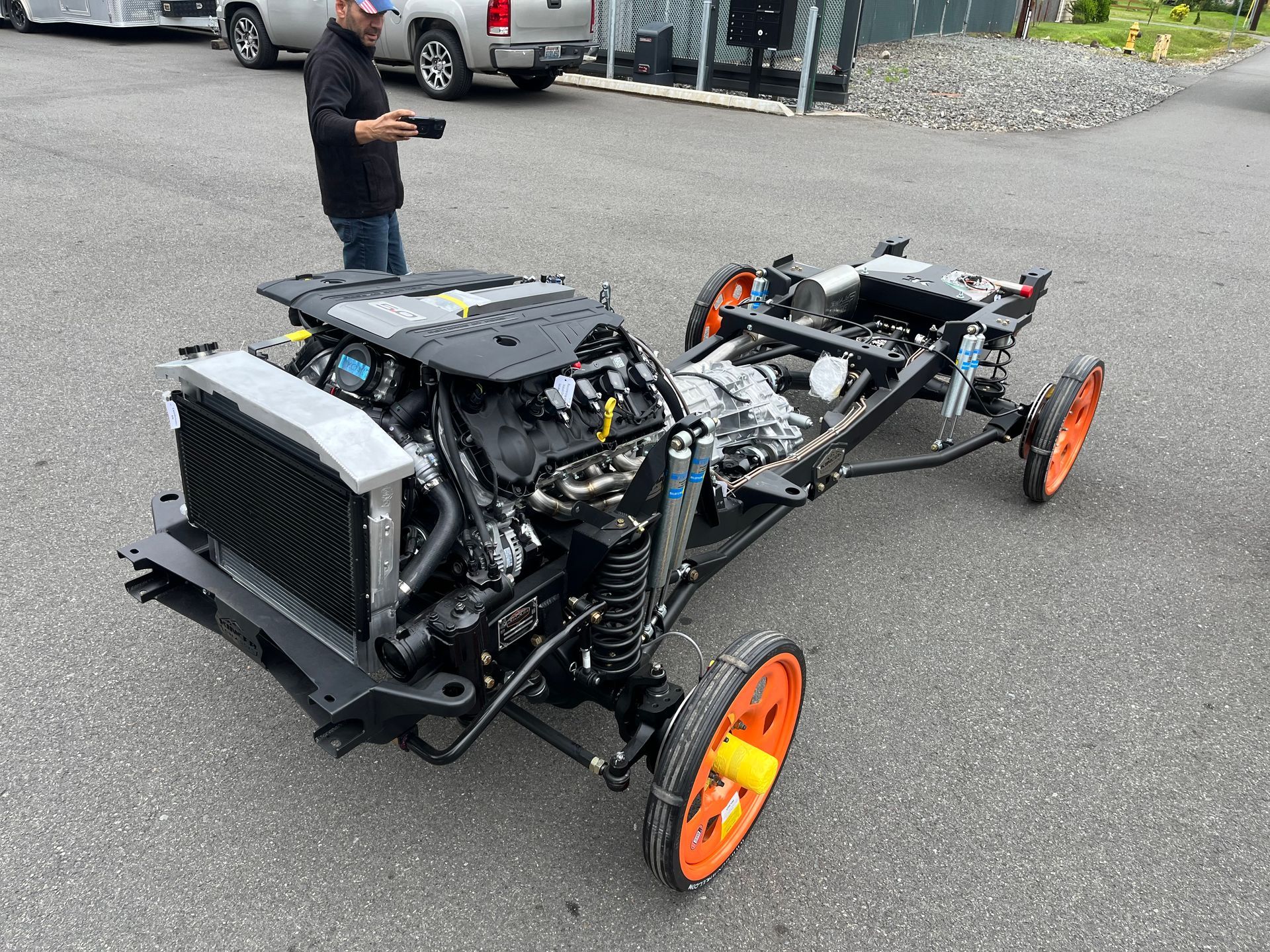 A man is standing next to a car chassis in a parking lot.