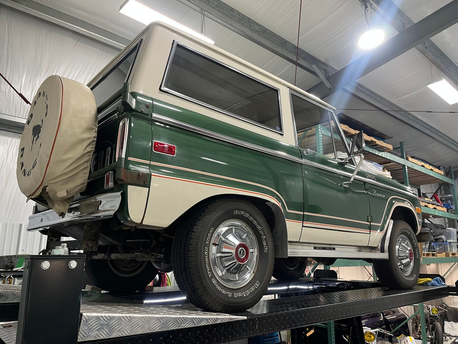 A green and white ford bronco is parked on a lift in a garage.