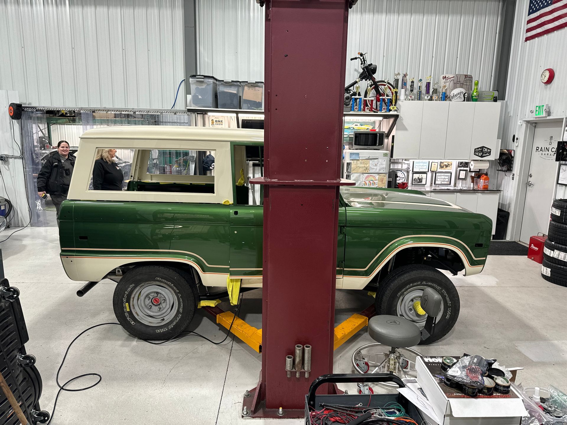 A green and white ford bronco is sitting on a lift in a garage.