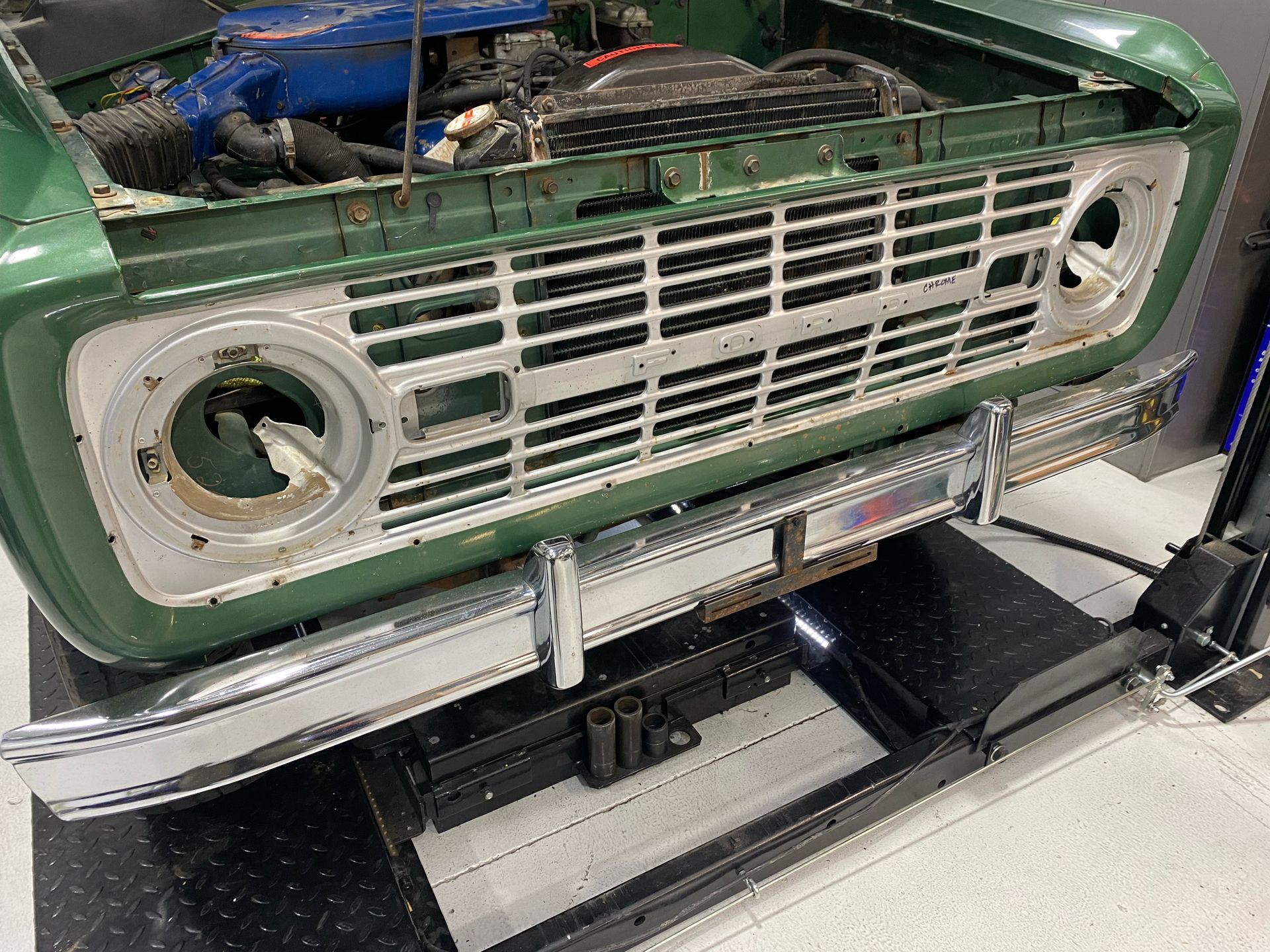 A green truck with the hood open is sitting on a lift.