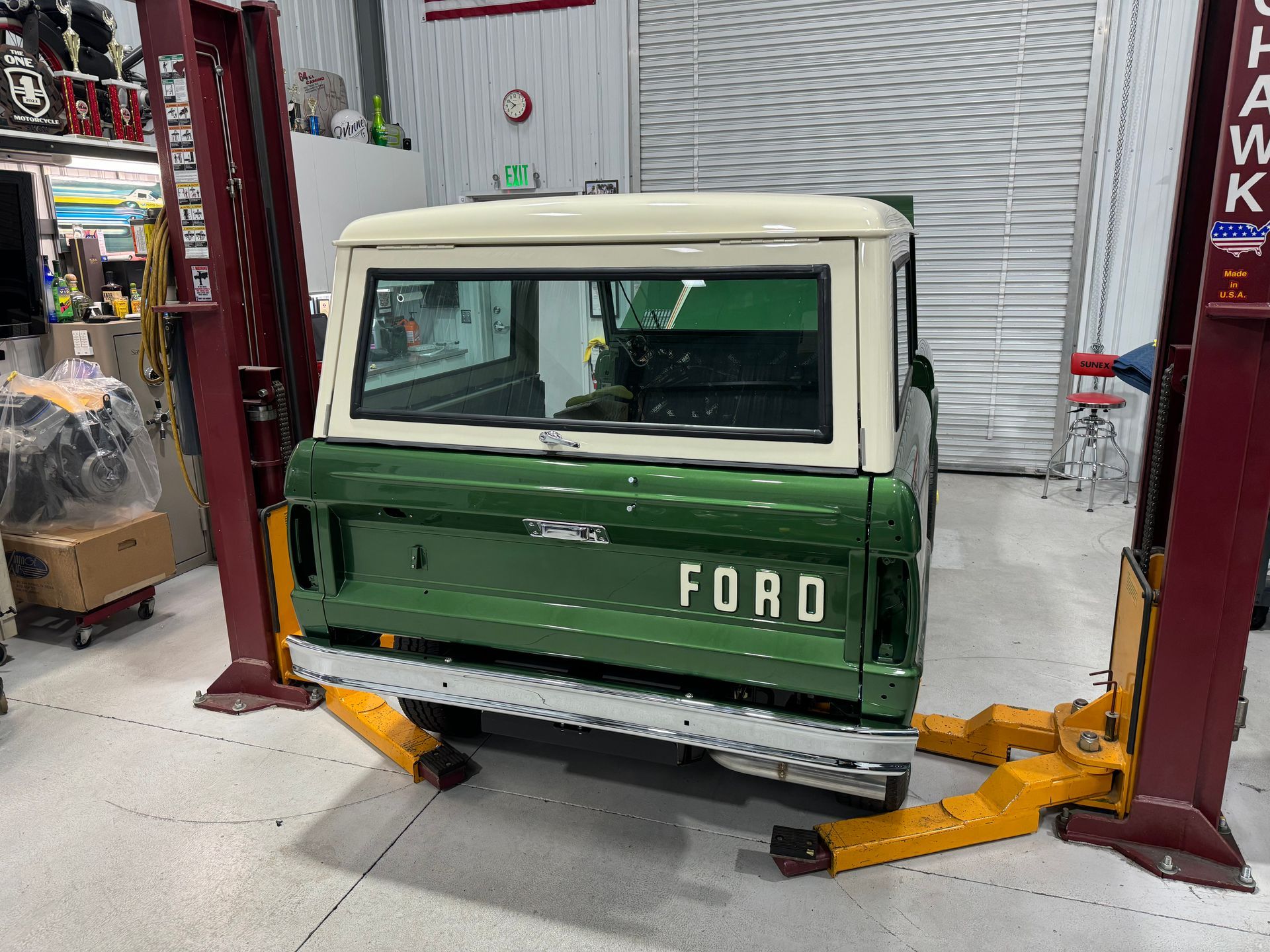 A green and white ford truck is on a lift in a garage.