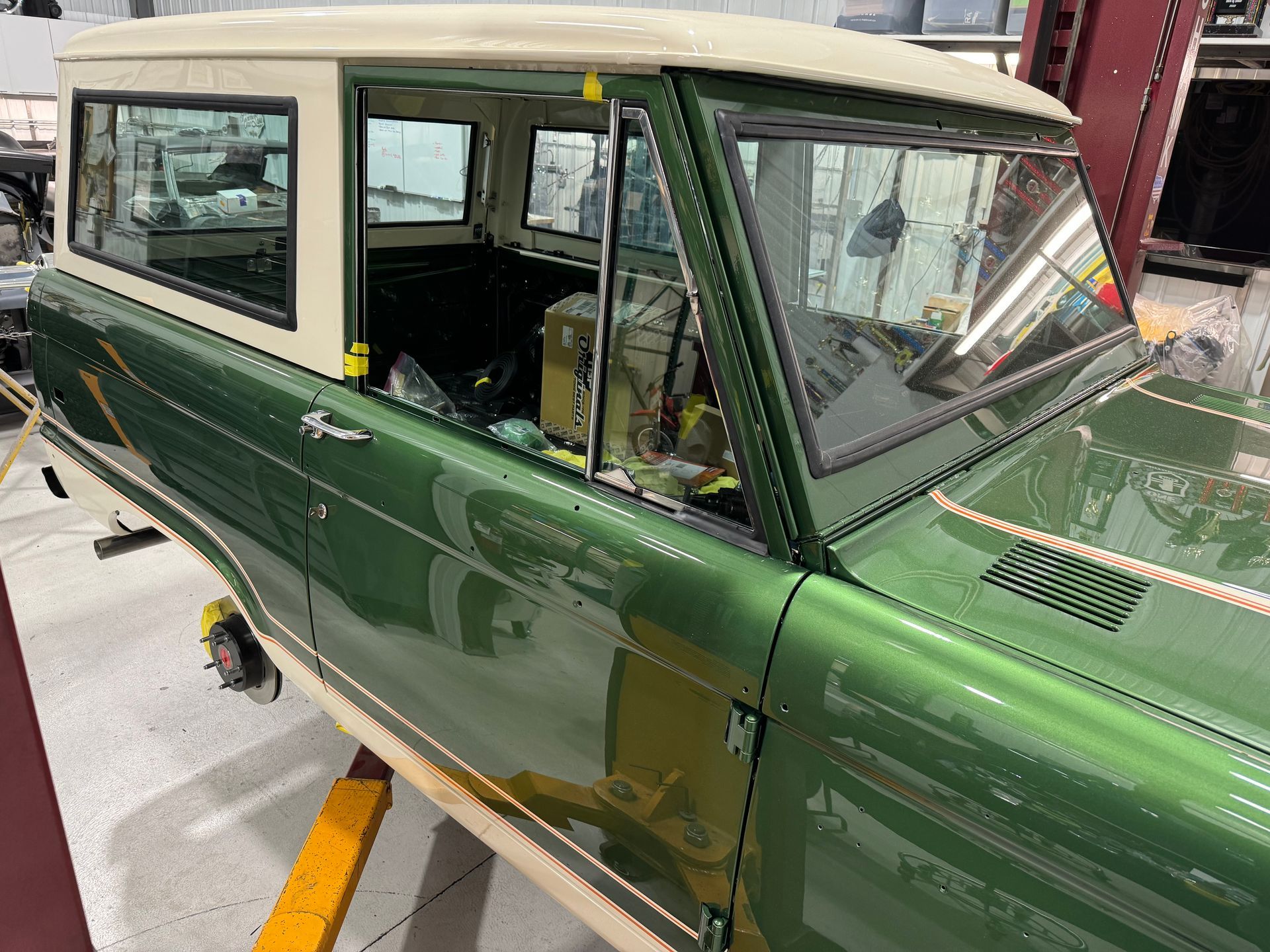 A green and white jeep is sitting on a lift in a garage.
