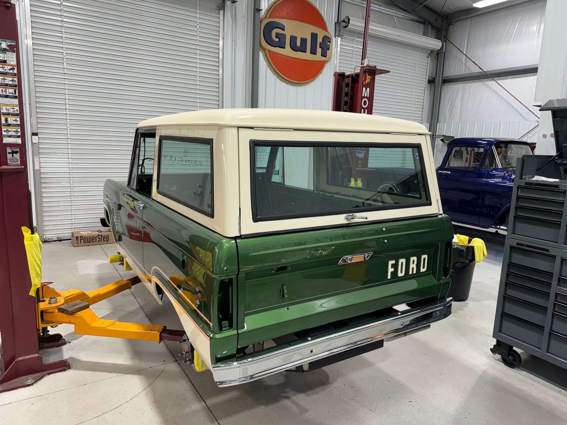 A green and white ford truck is sitting on a lift in a garage.