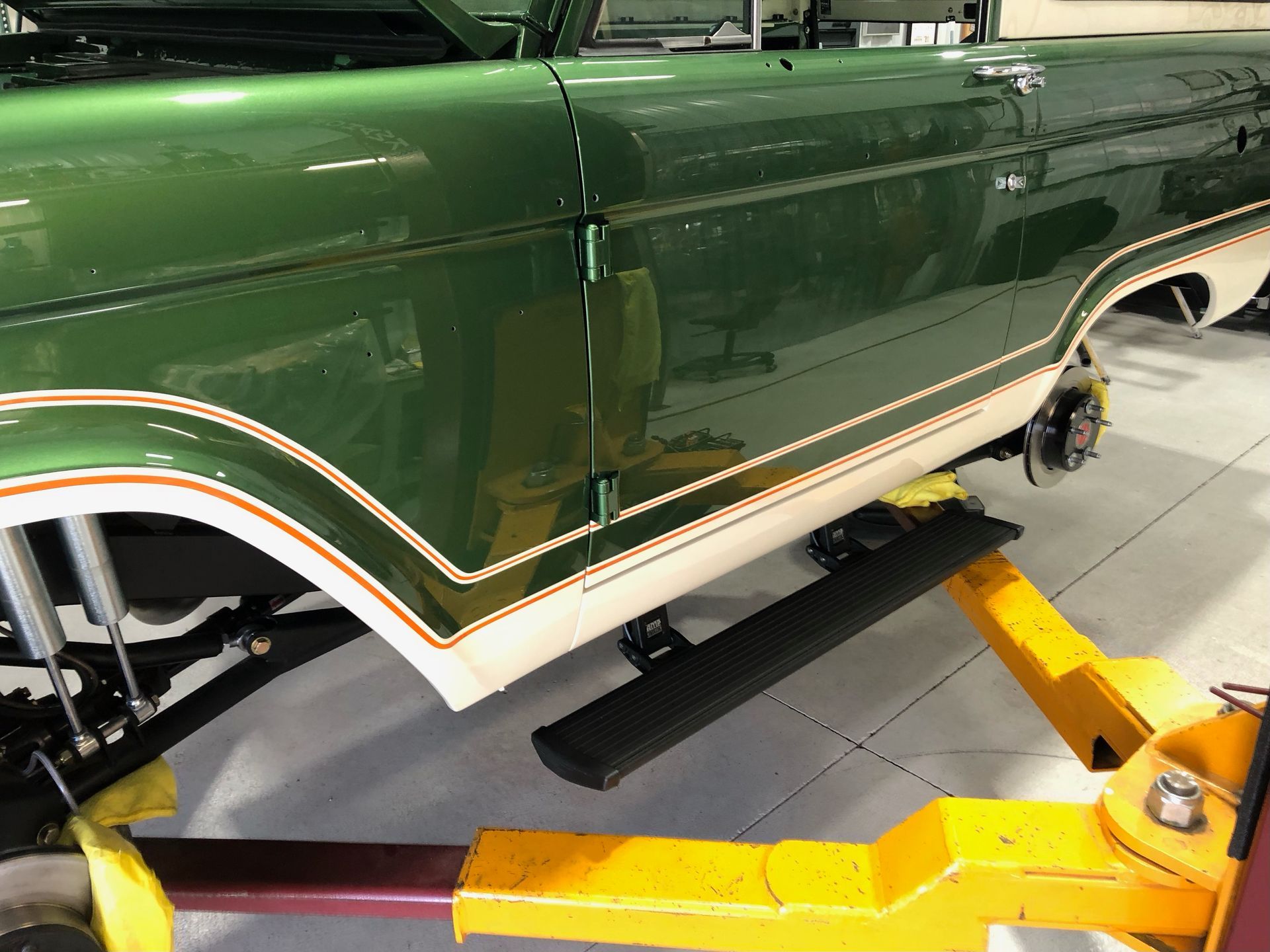 A green truck is sitting on a yellow lift in a garage.