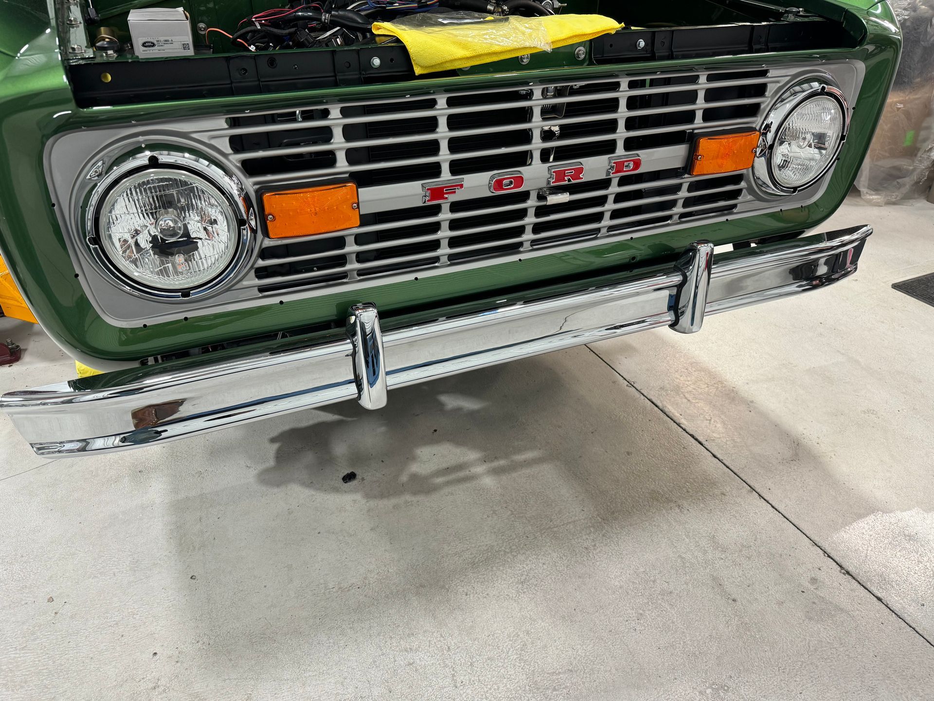 A green truck with the hood up is parked in a garage.