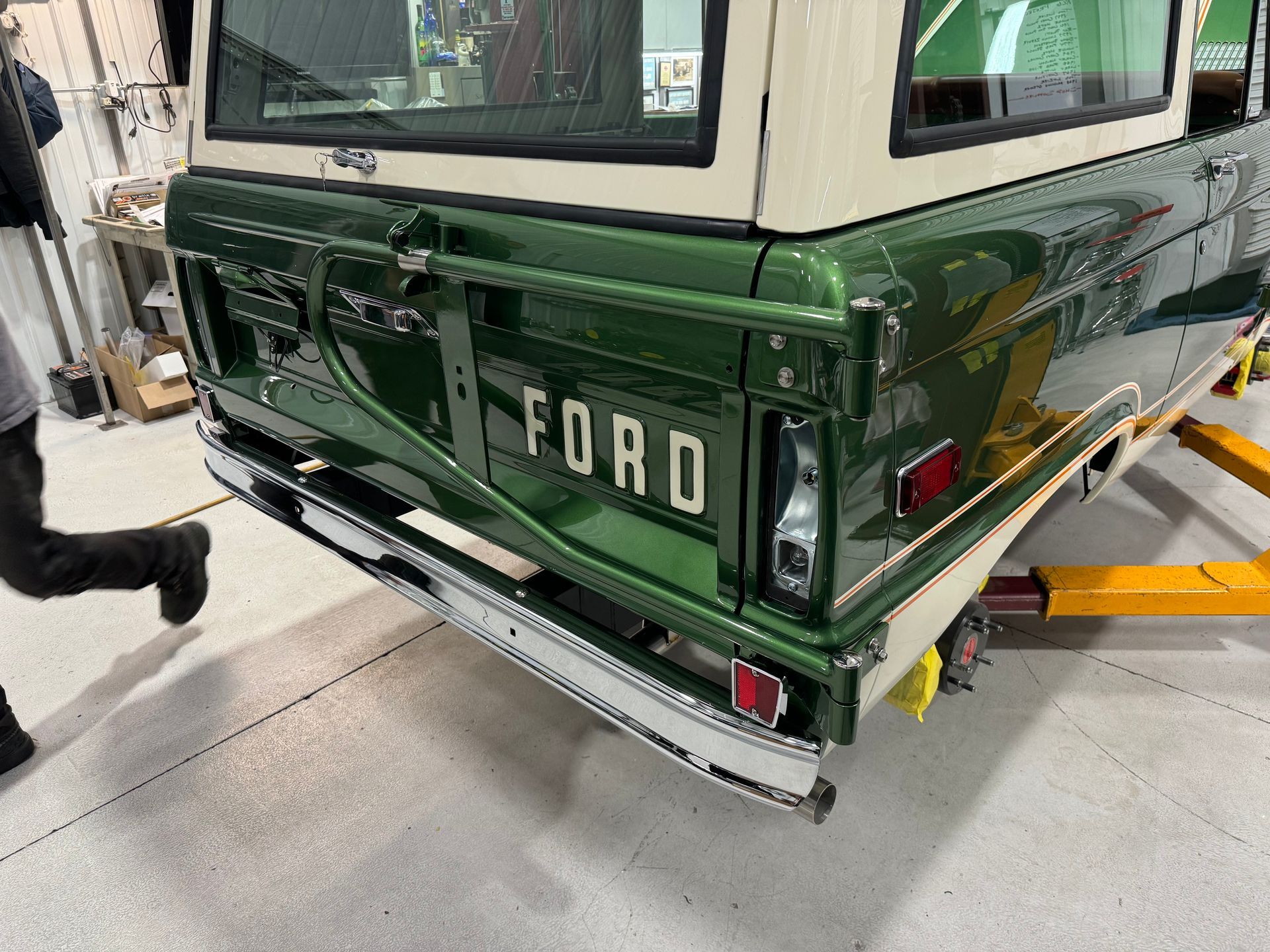 A green and white ford bronco is sitting on a lift in a garage.