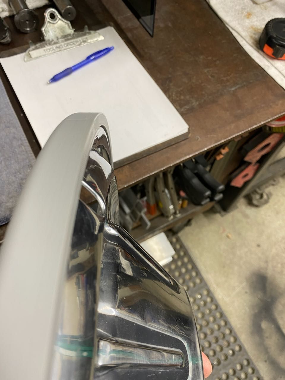 A person is holding a metal object in front of a clipboard with a pen on it.