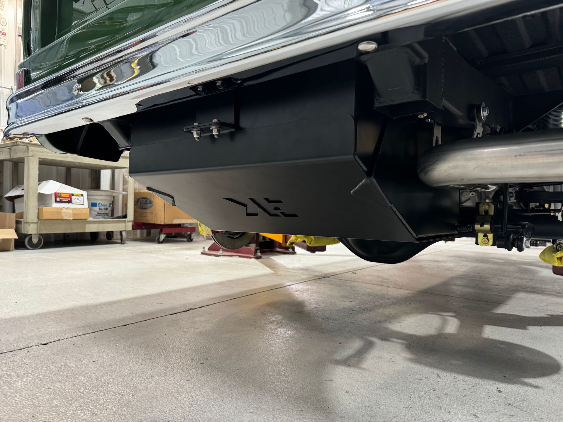 A green truck is parked in a garage with a black exhaust pipe.