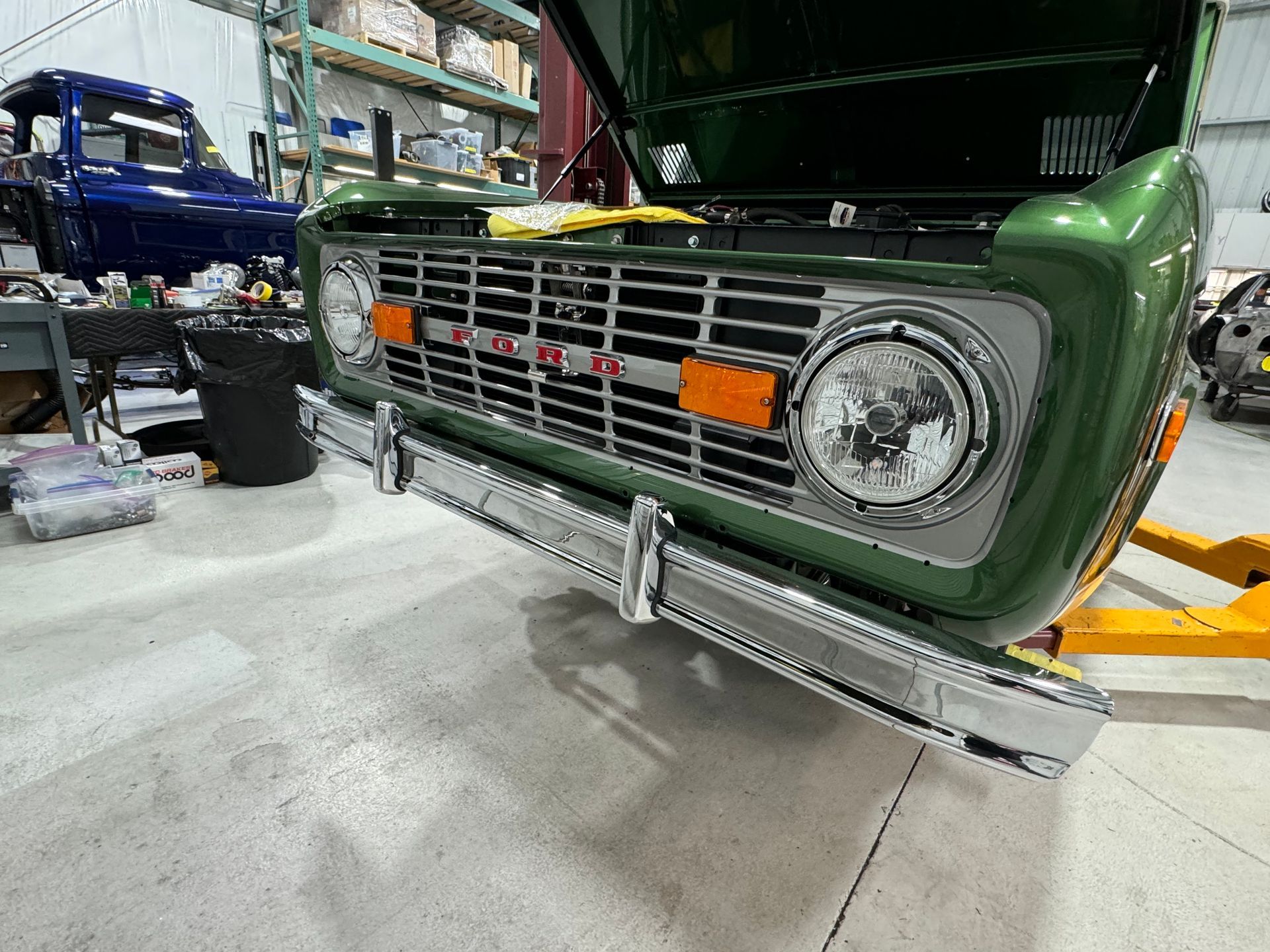 A green truck with the hood open is sitting on a lift in a garage.