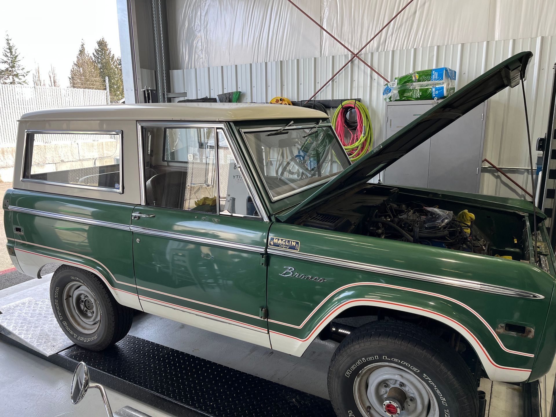 A green jeep with the hood up is parked in a garage.