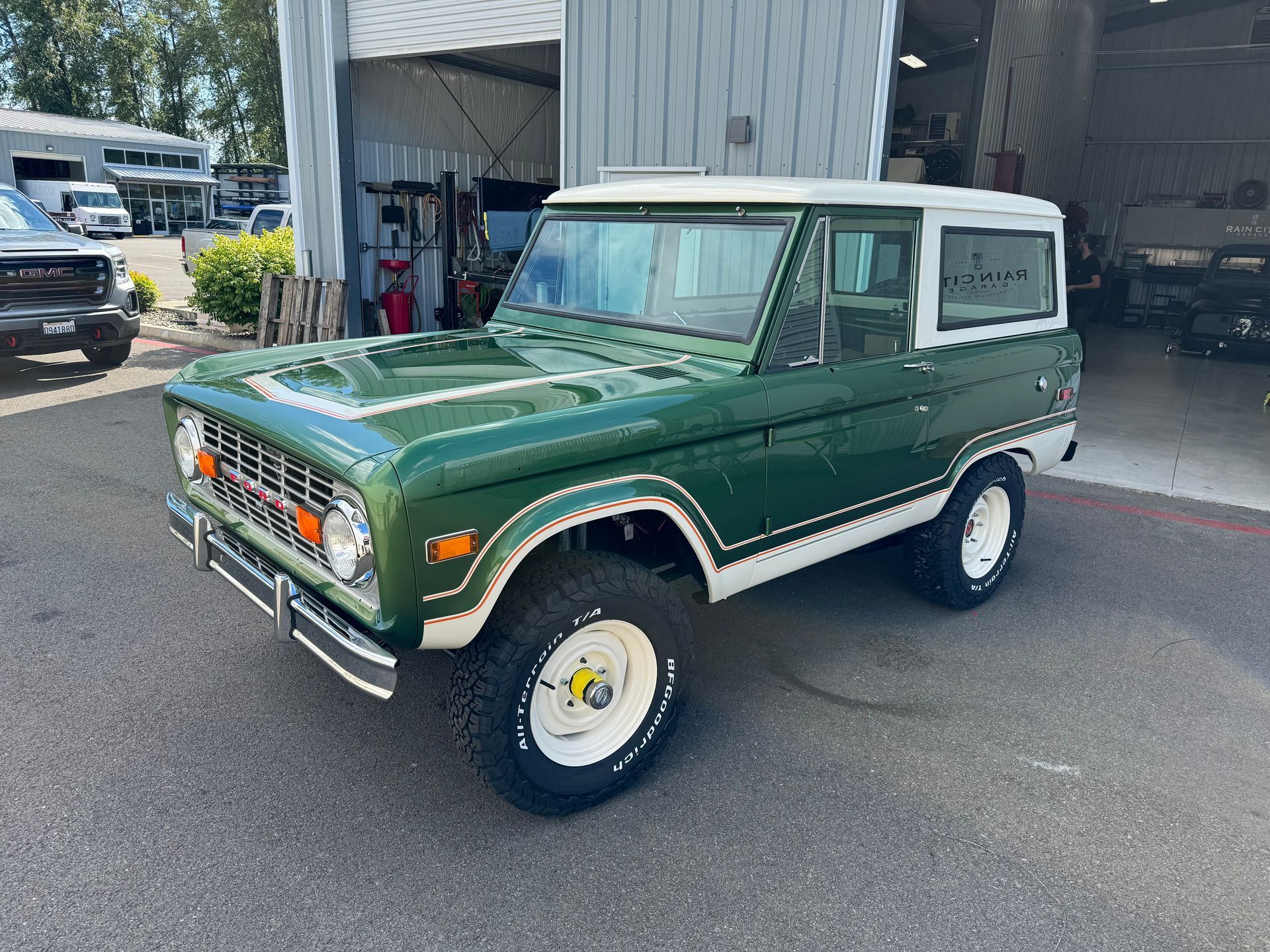 A green and white ford bronco is parked in front of a garage.