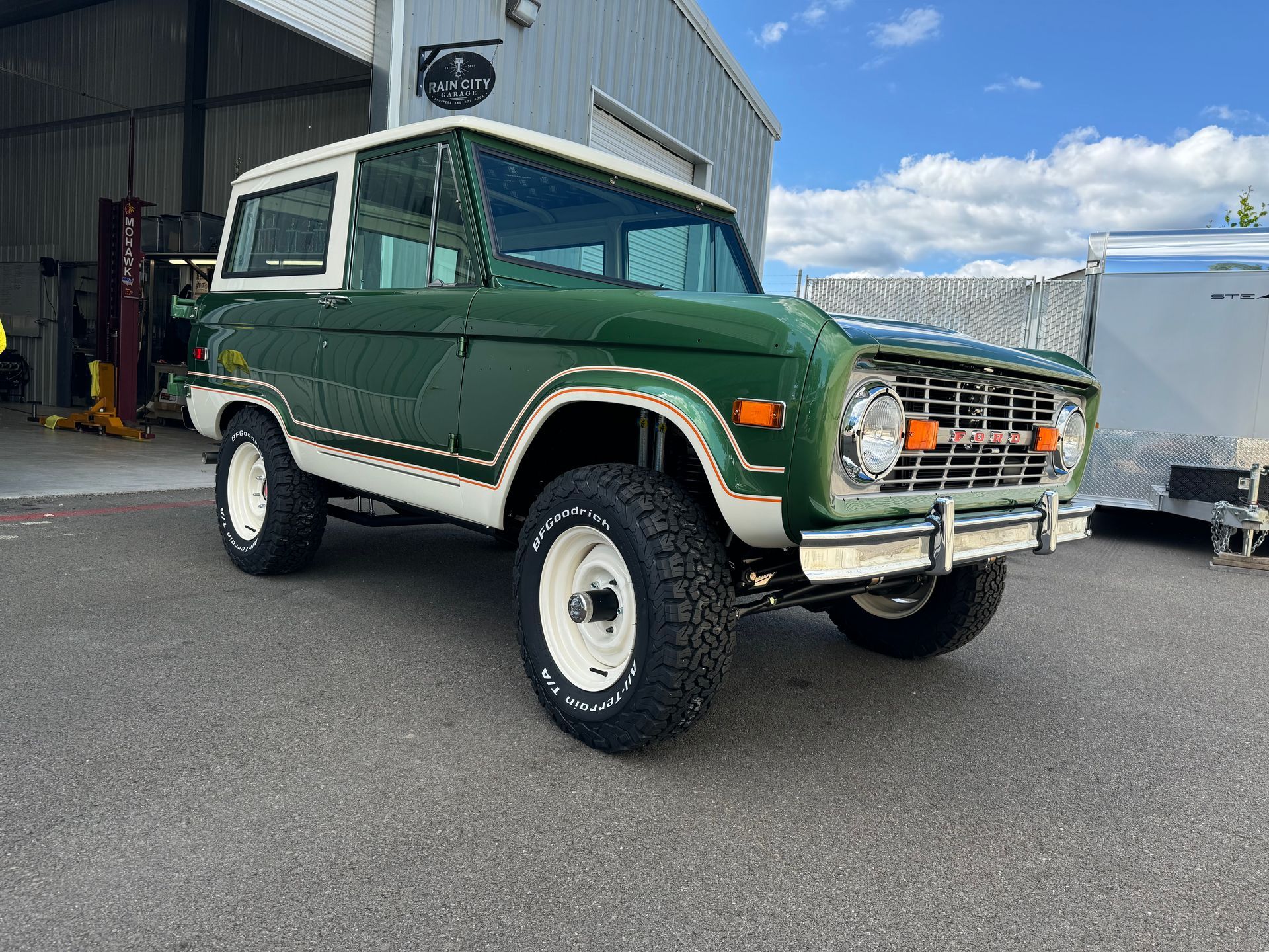 A green and white ford bronco is parked in front of a garage.