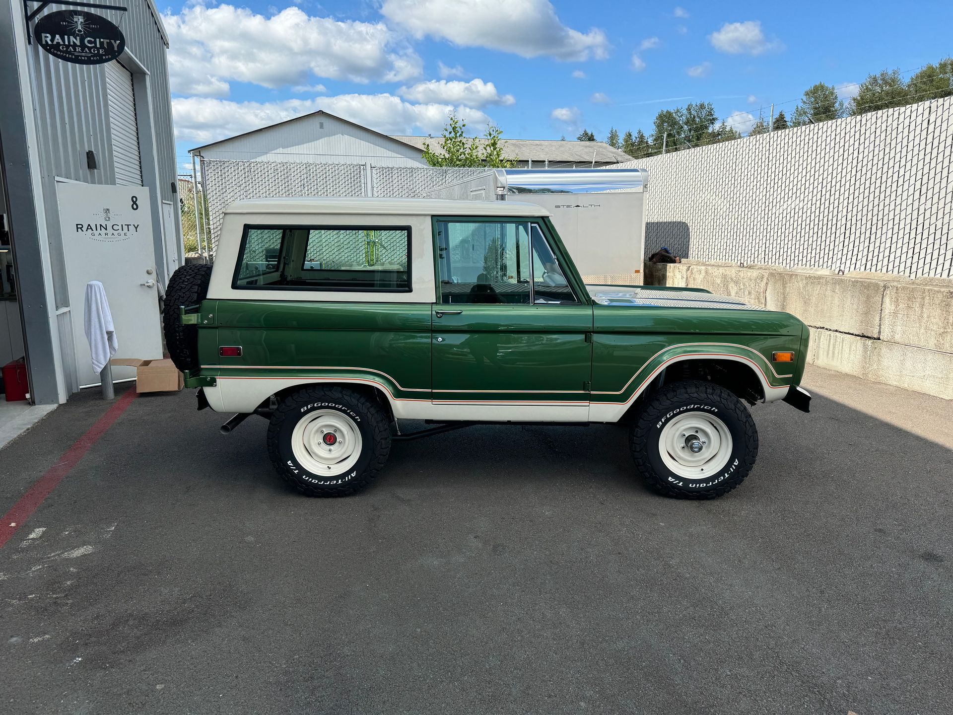A green and white ford bronco is parked in front of a building.