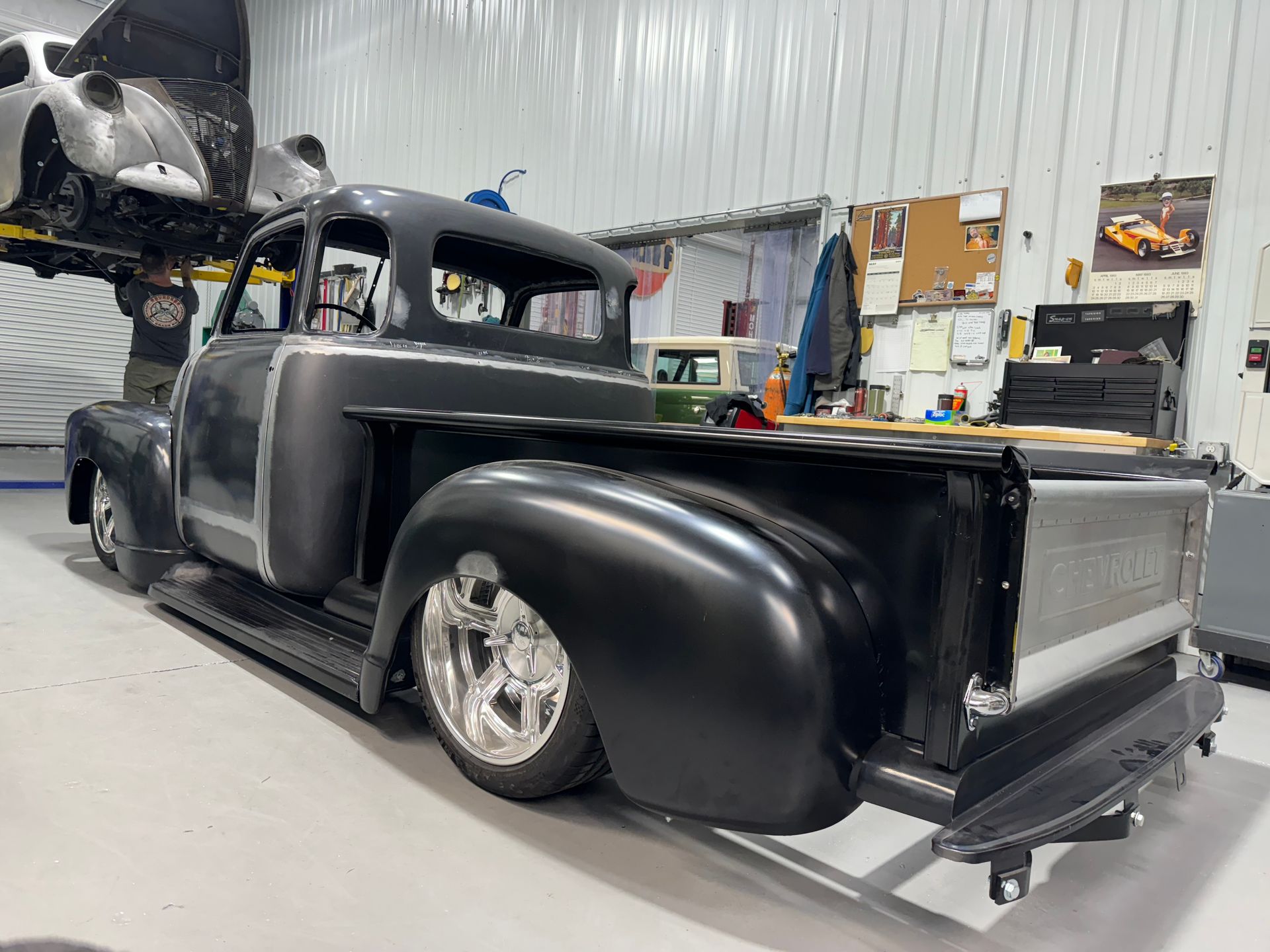A black truck is parked in a garage next to a car.