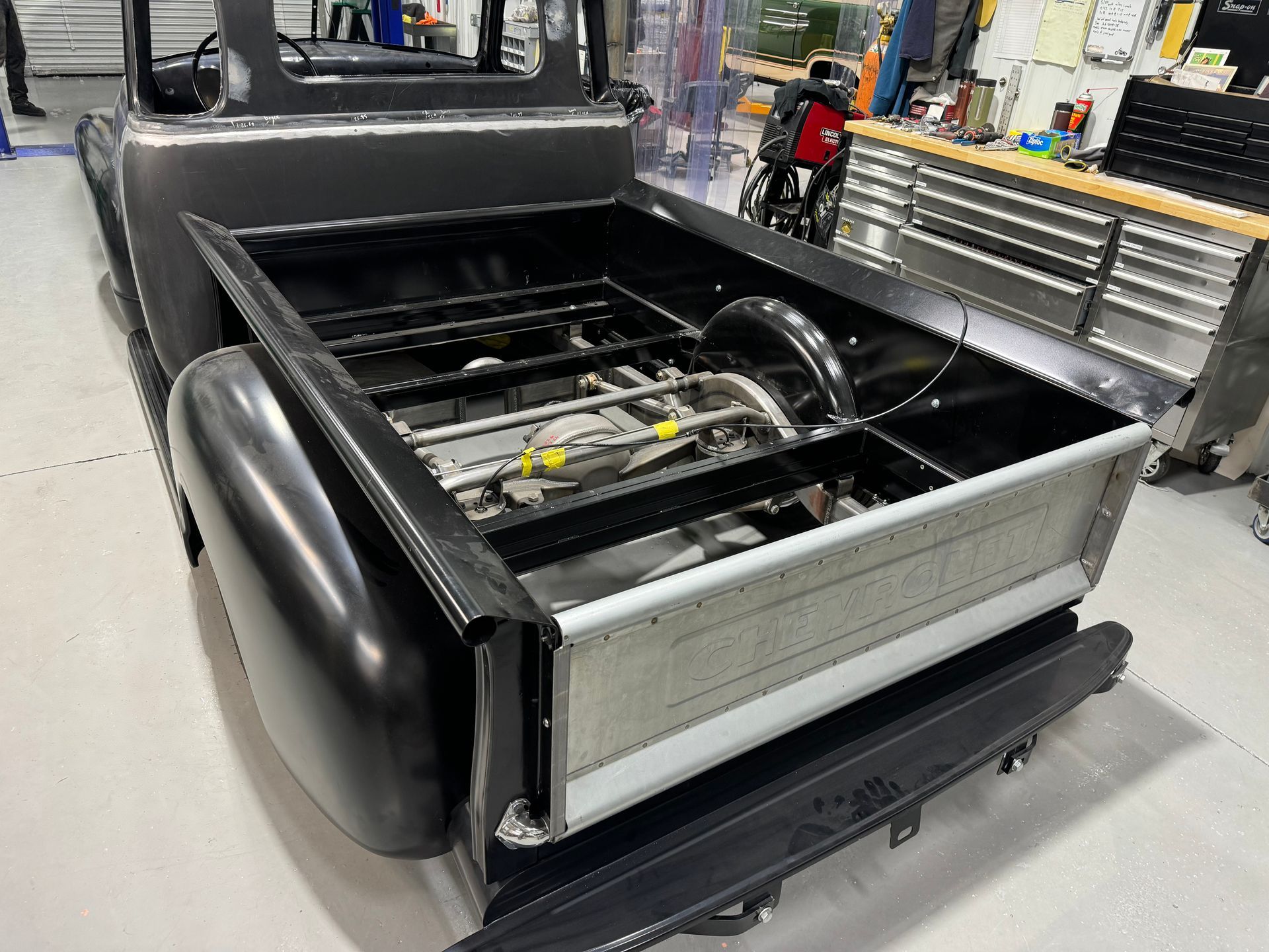 A black truck is sitting in a garage with the bed open.