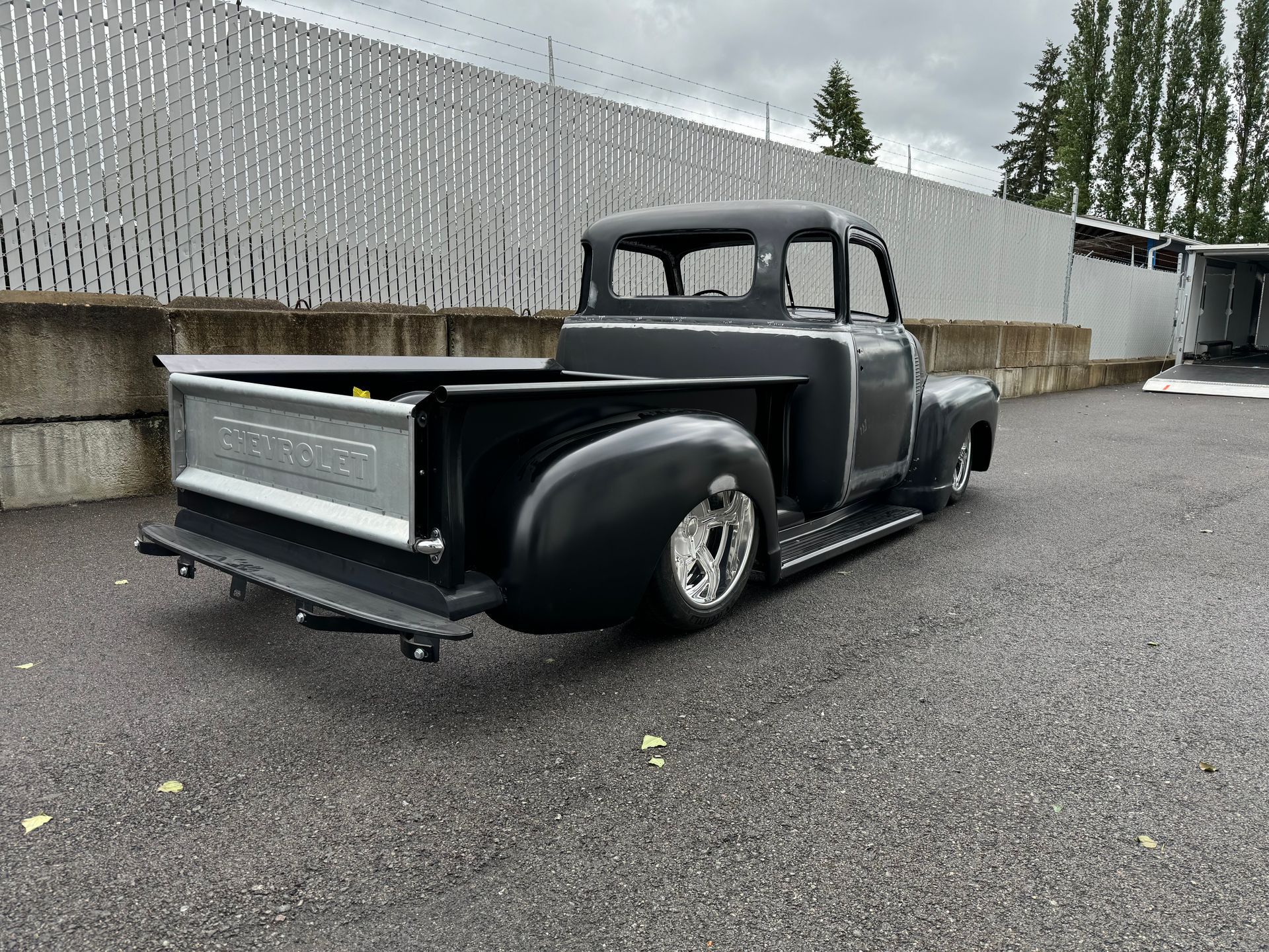 A black truck is parked in a parking lot next to a fence.