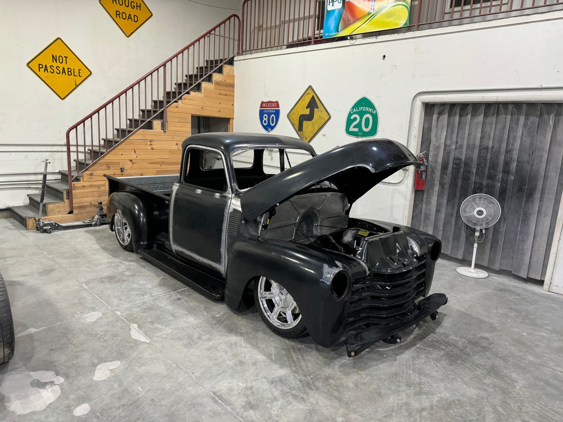 A black truck with the hood up is parked in a garage.