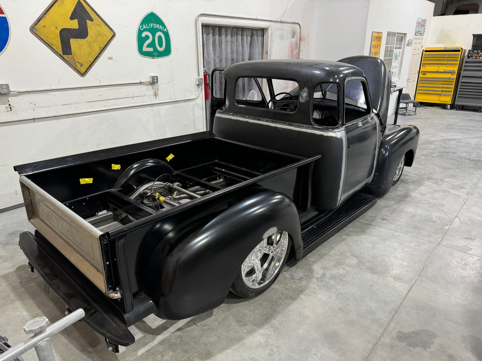 A black truck is parked in a garage with a highway sign on the wall.