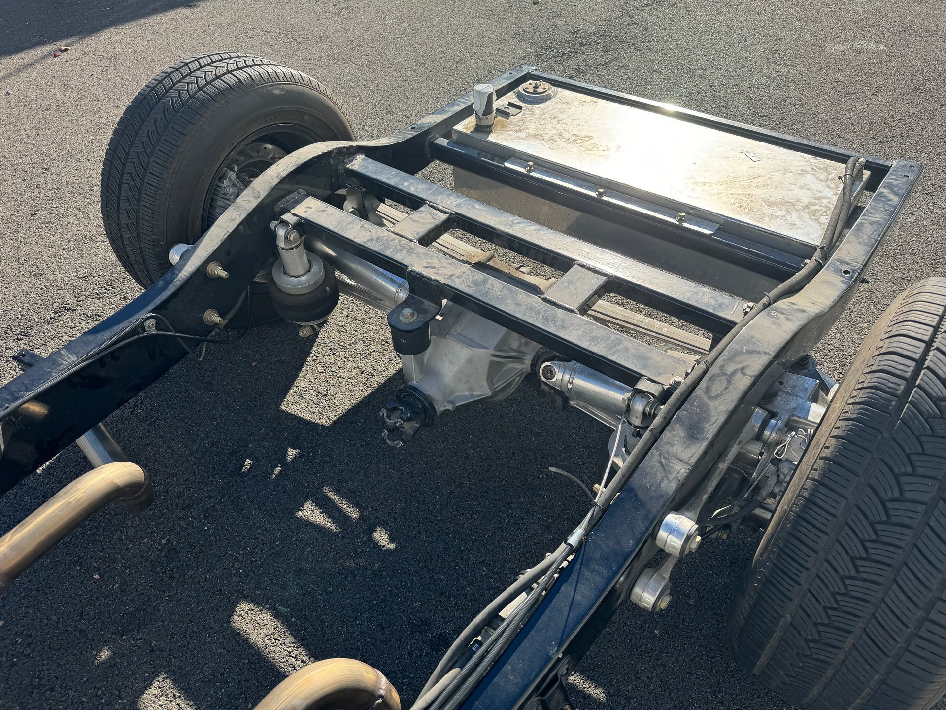 A truck frame is sitting on the ground next to a tire.