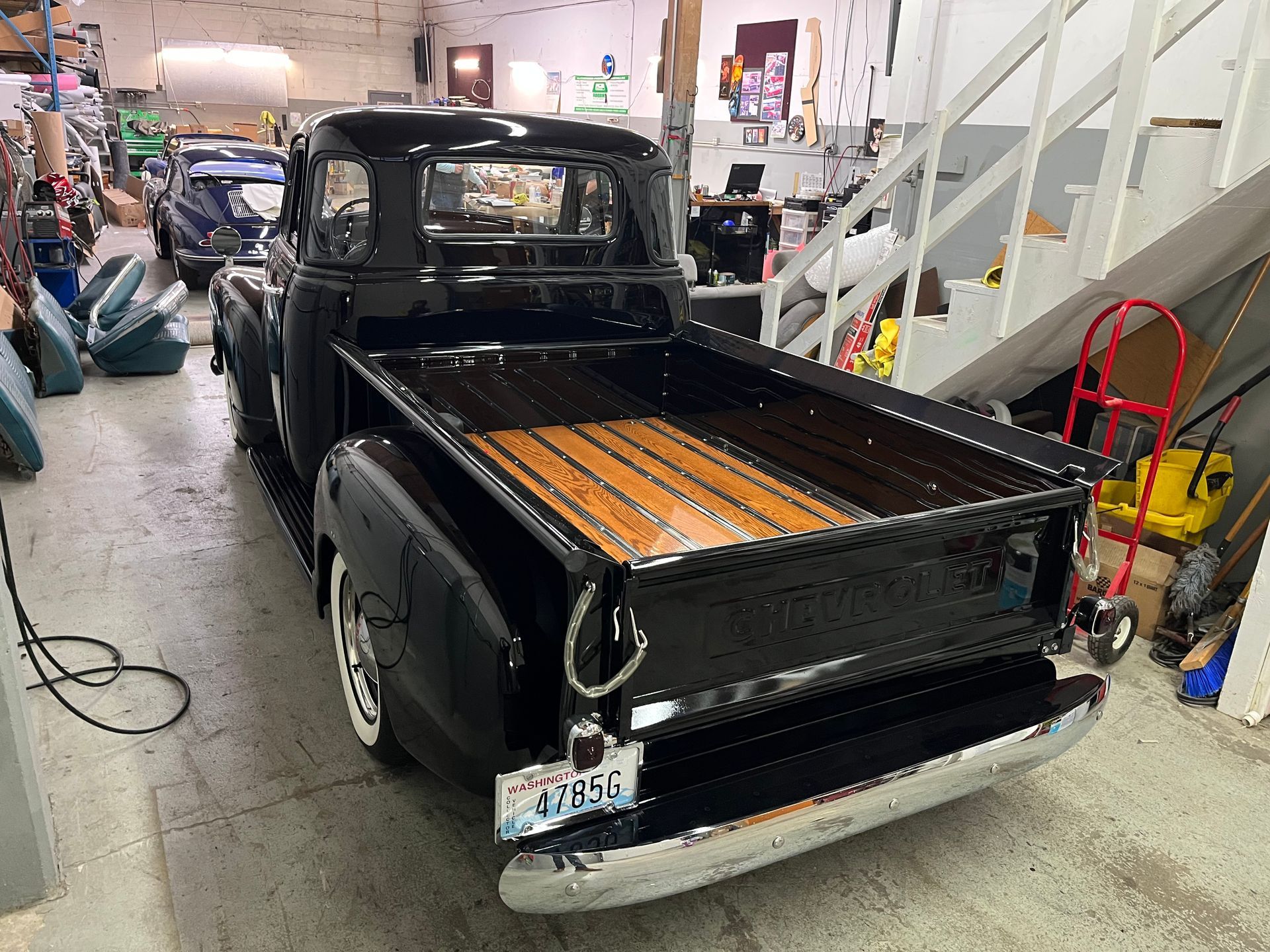 A black truck with a wooden bed is parked in a garage.
