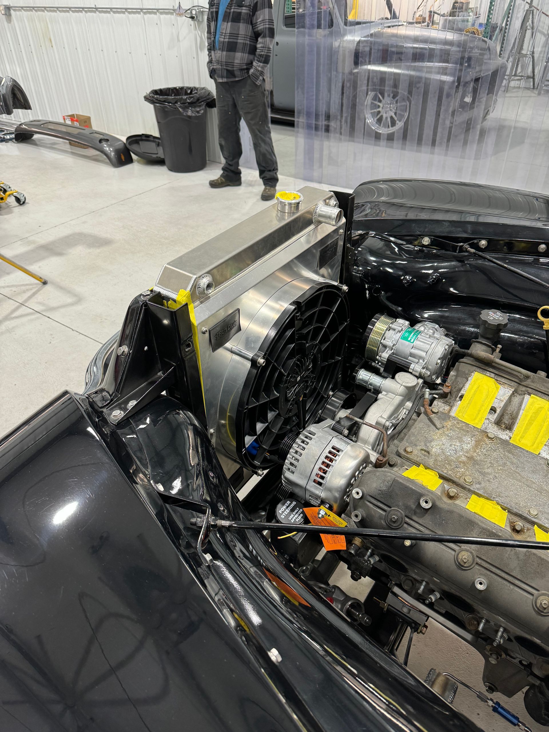 A man is standing next to a black car with the hood open.