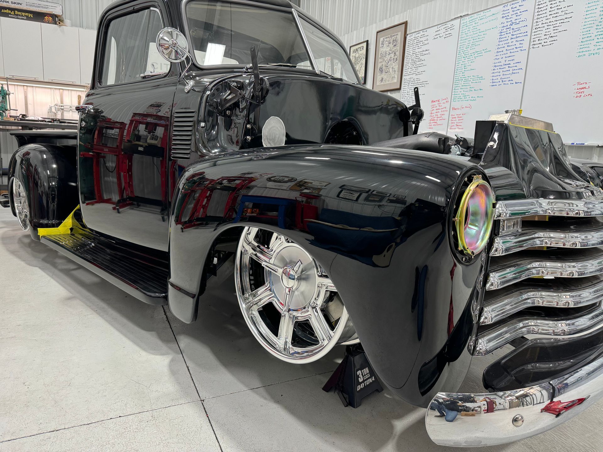 A black truck is parked in a garage next to a white board.