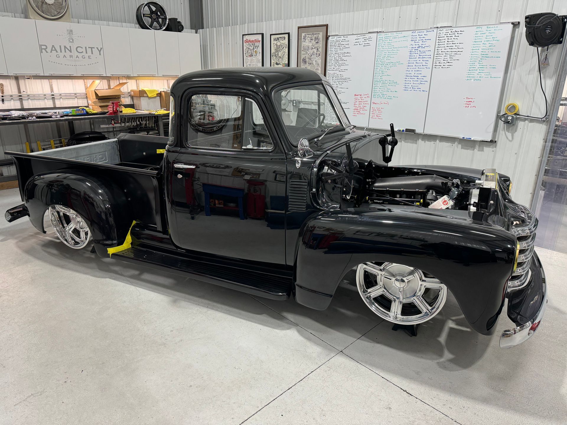 A black truck is parked in a garage with the hood open.