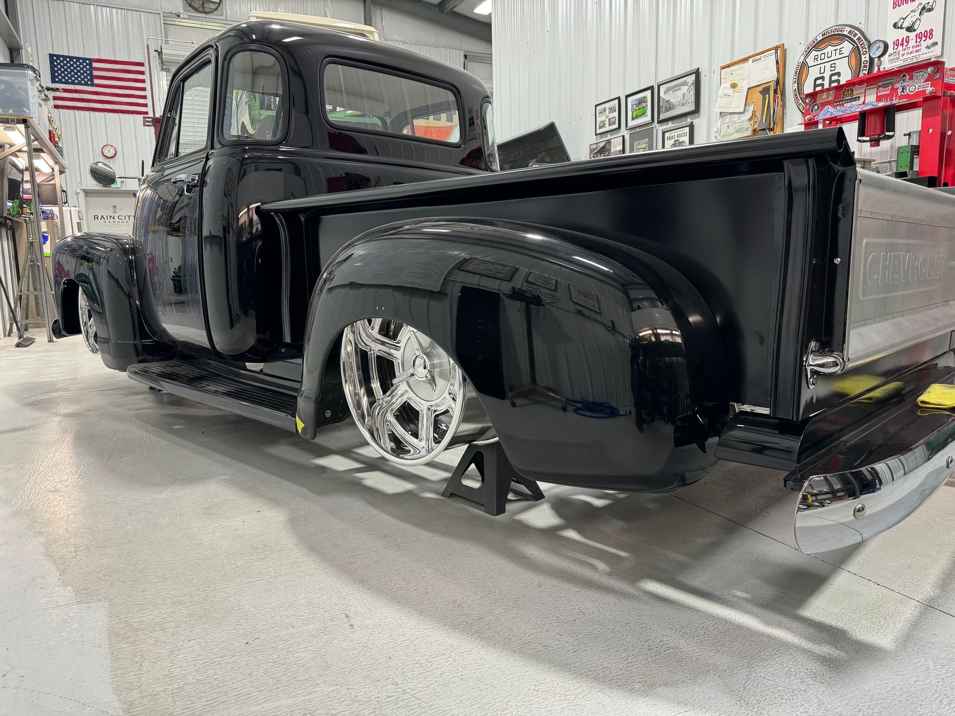 A black truck is sitting on a jack in a garage.