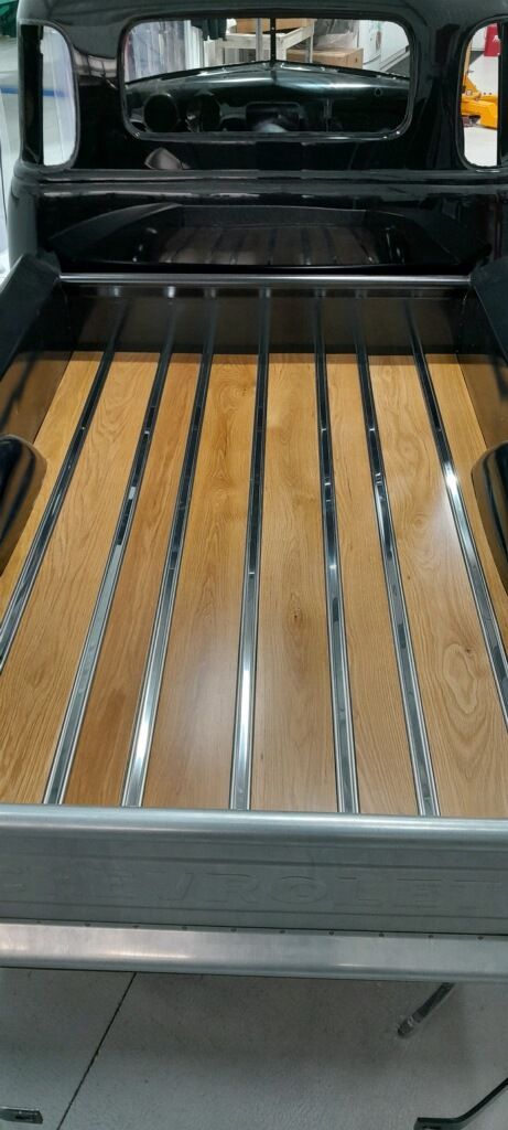 The back of a truck with a wooden bed and metal tracks.