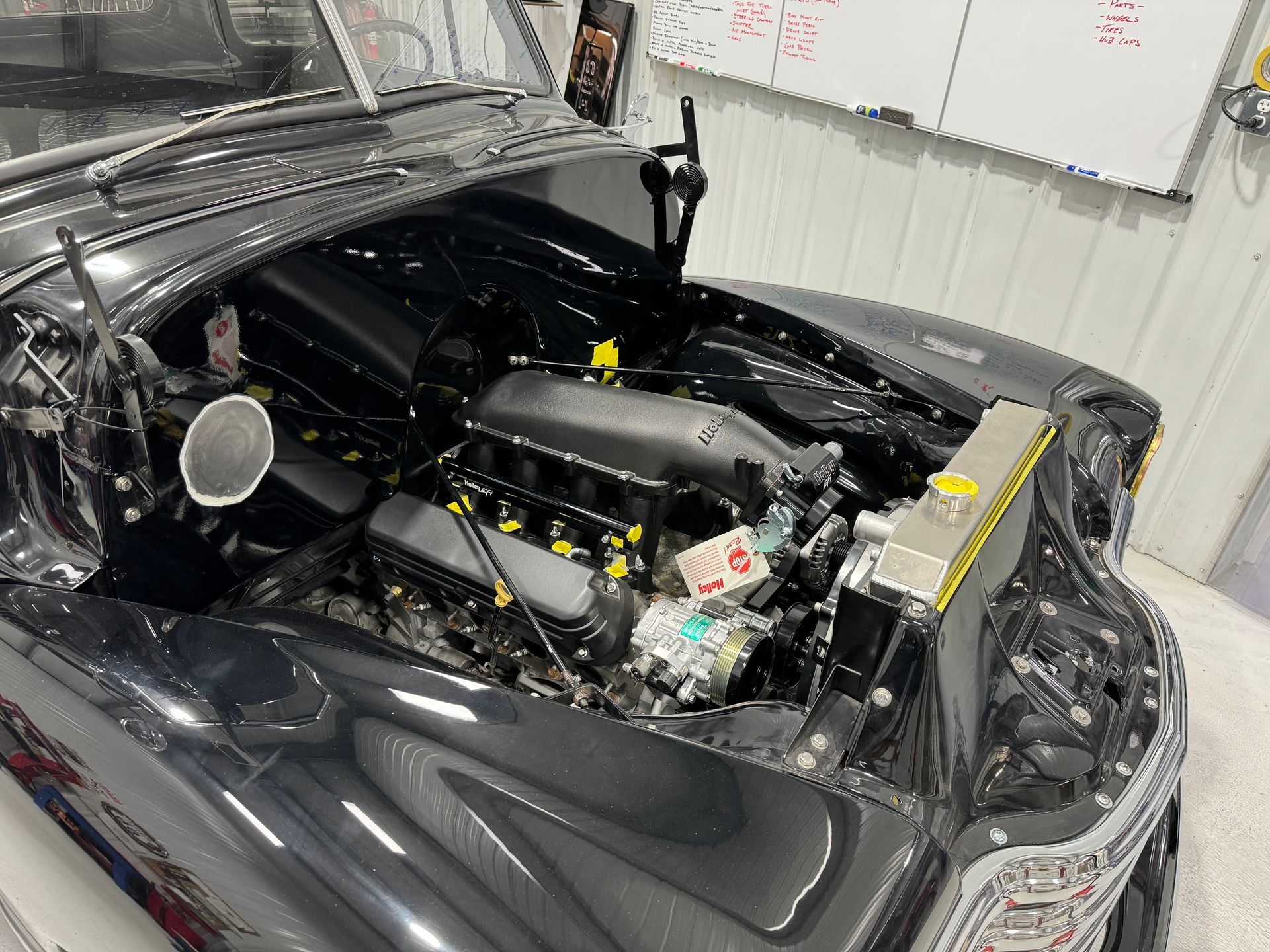 A black car with the hood open is sitting in a garage.