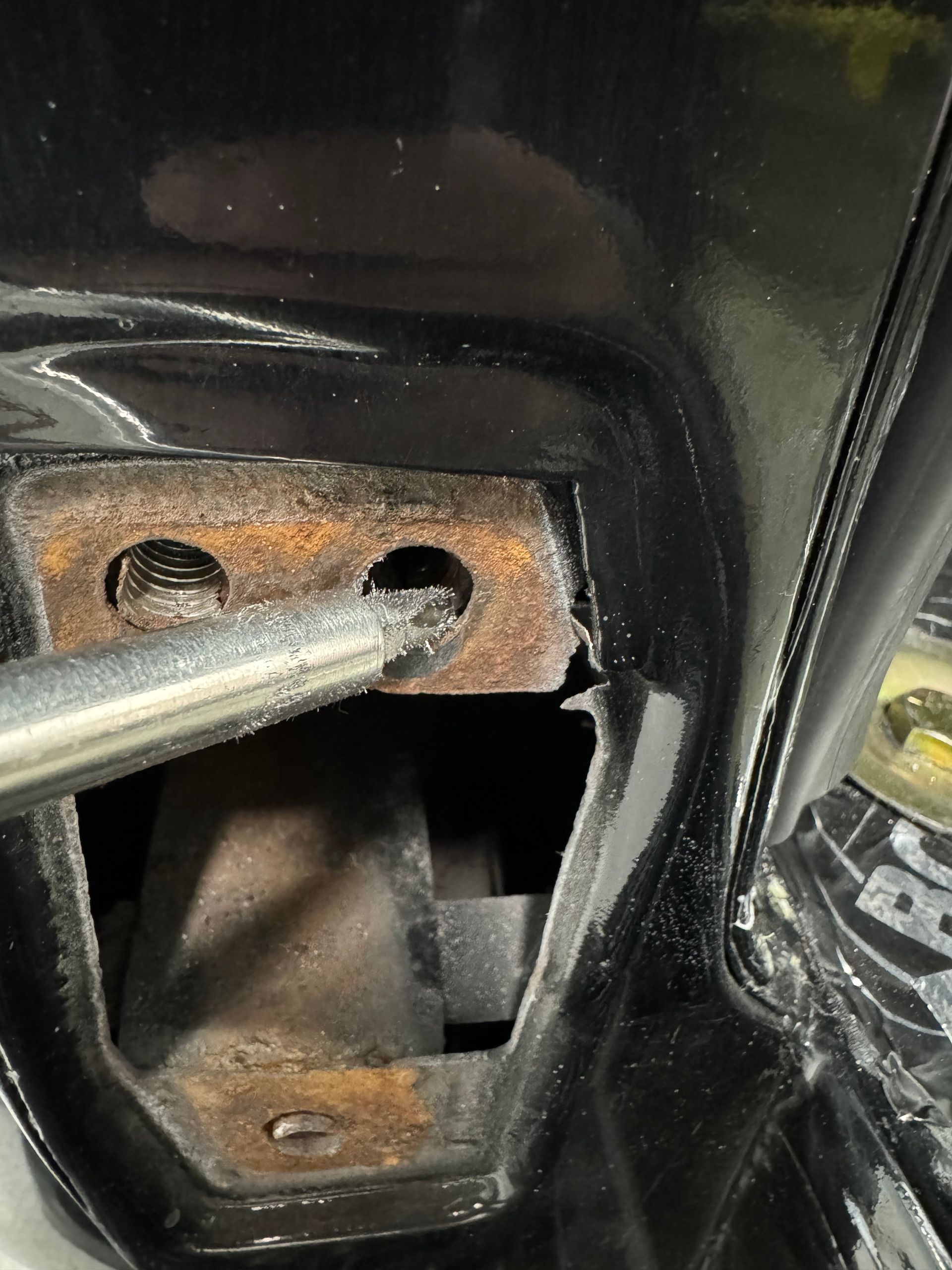 A person is using a screwdriver to remove a rusty piece of metal from a car.