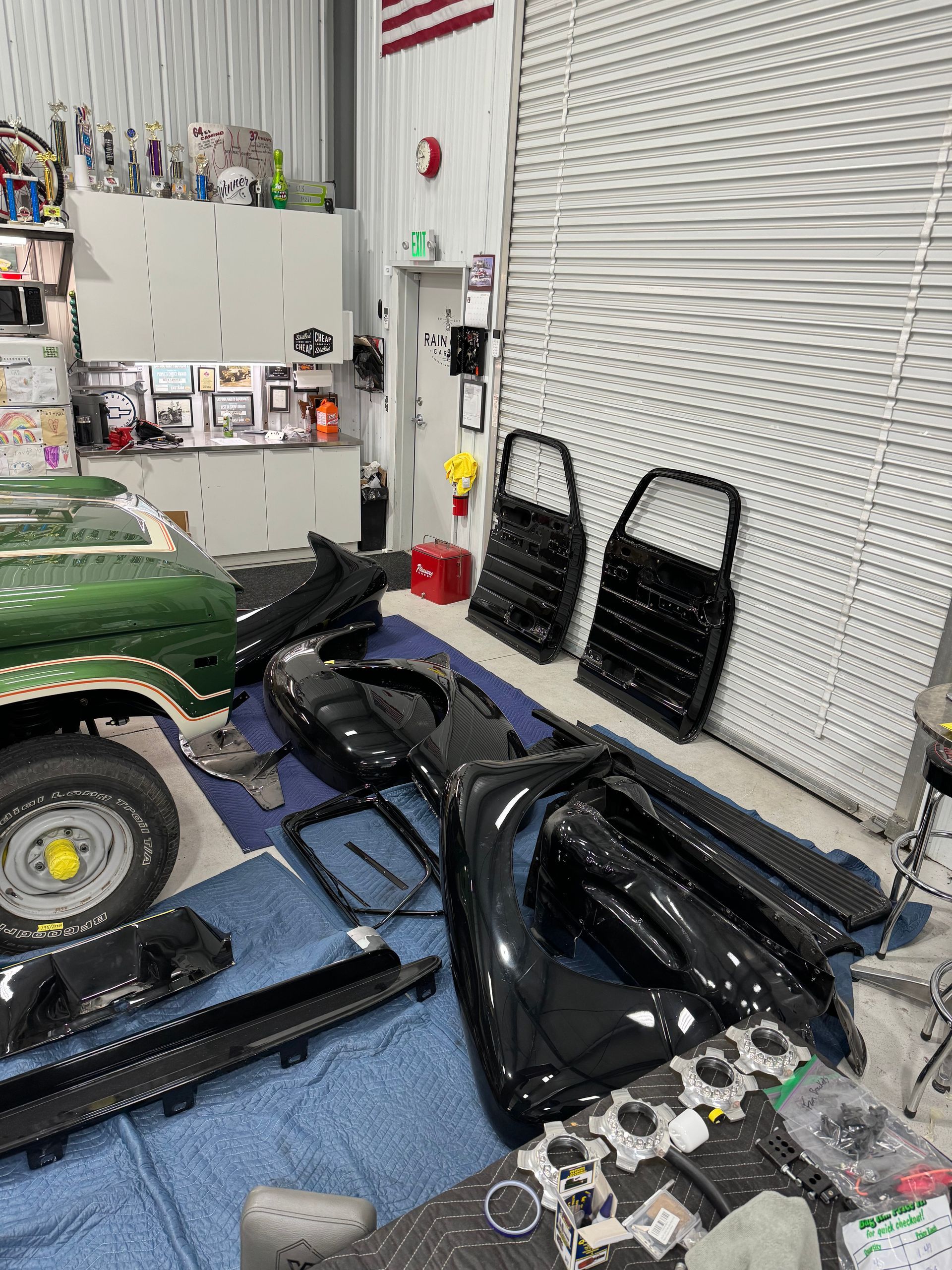 A green car is sitting in a garage with a lot of parts on the floor.