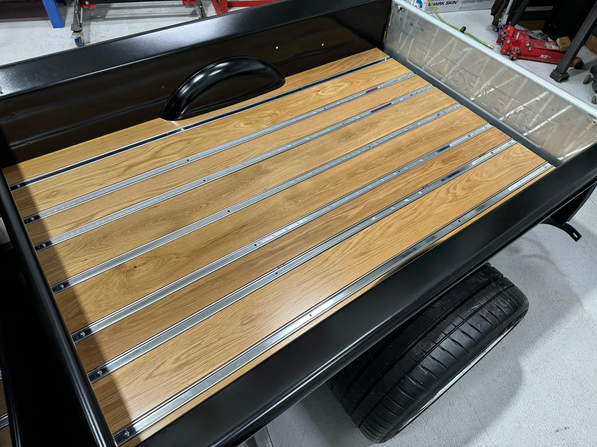 The back of a truck with a wooden bed and a tire.