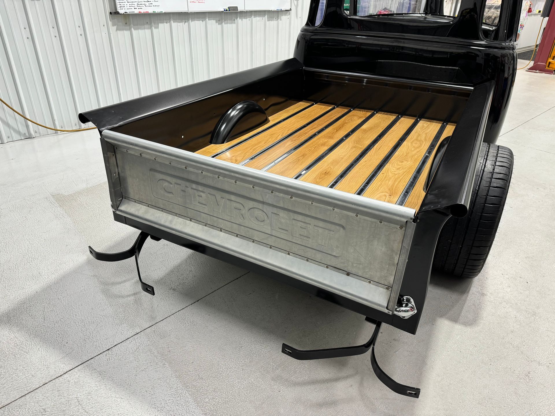 A black truck with a wooden bed is parked in a garage.
