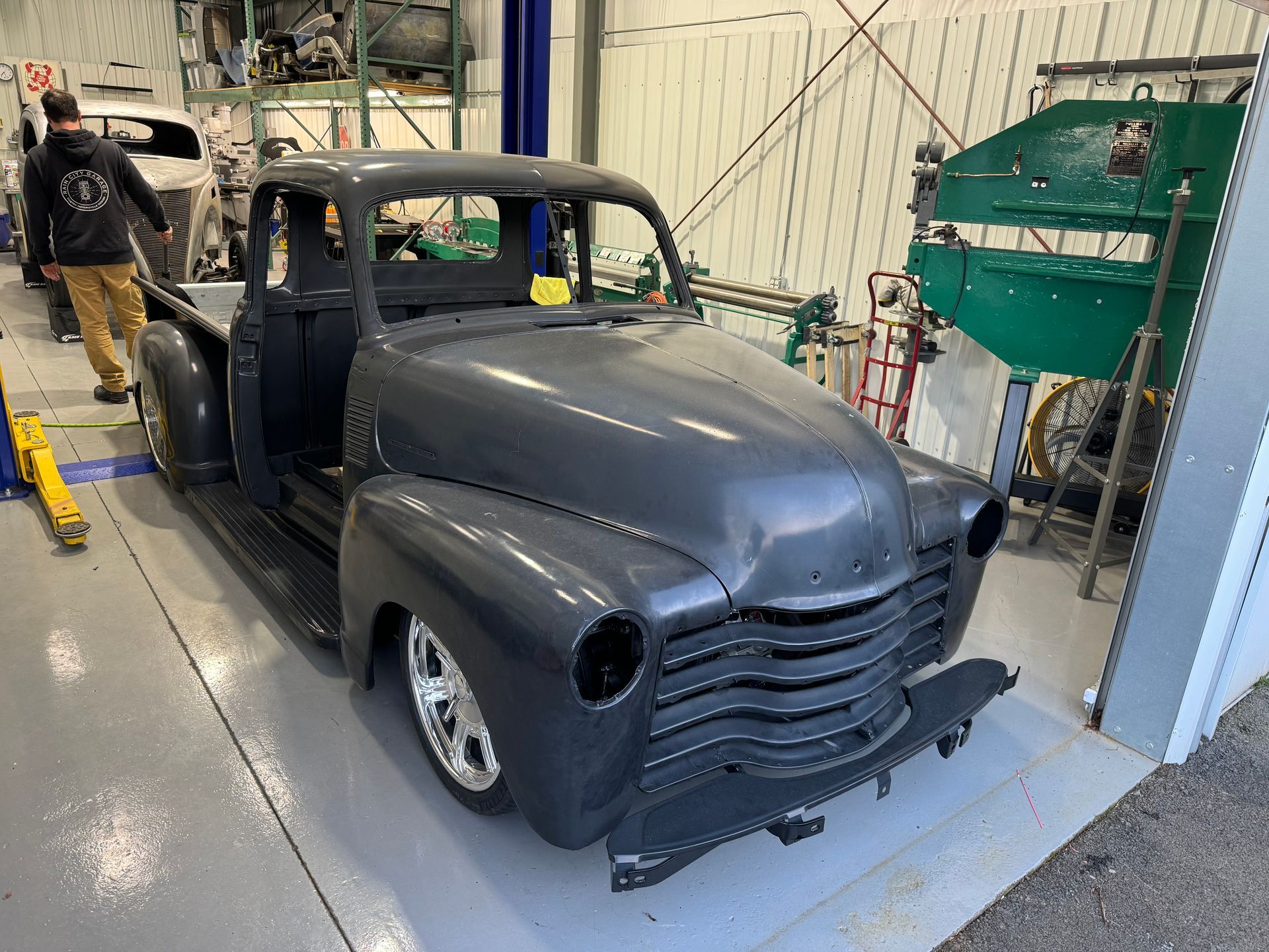 A gray truck is sitting in a garage with a man standing behind it.