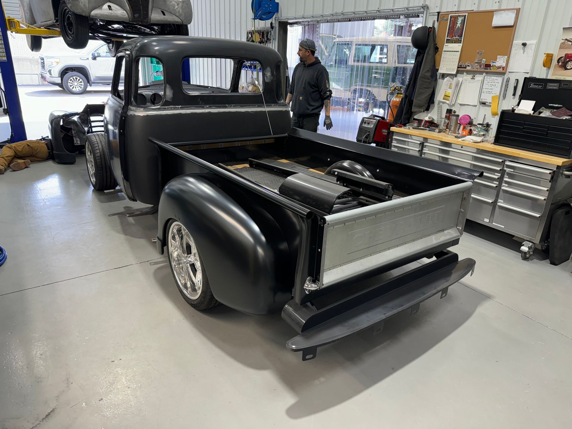 A man is standing next to a black truck in a garage.