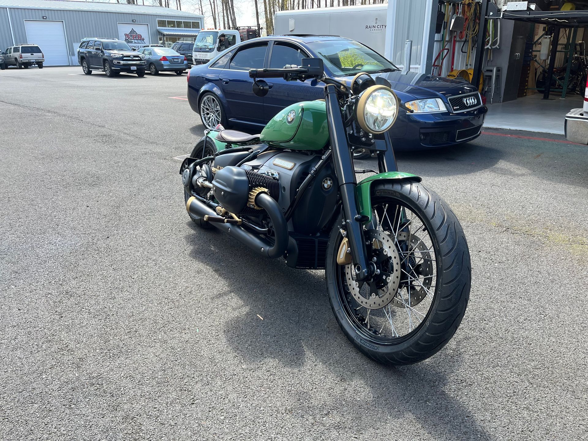 A green motorcycle is parked in a parking lot next to a blue car.