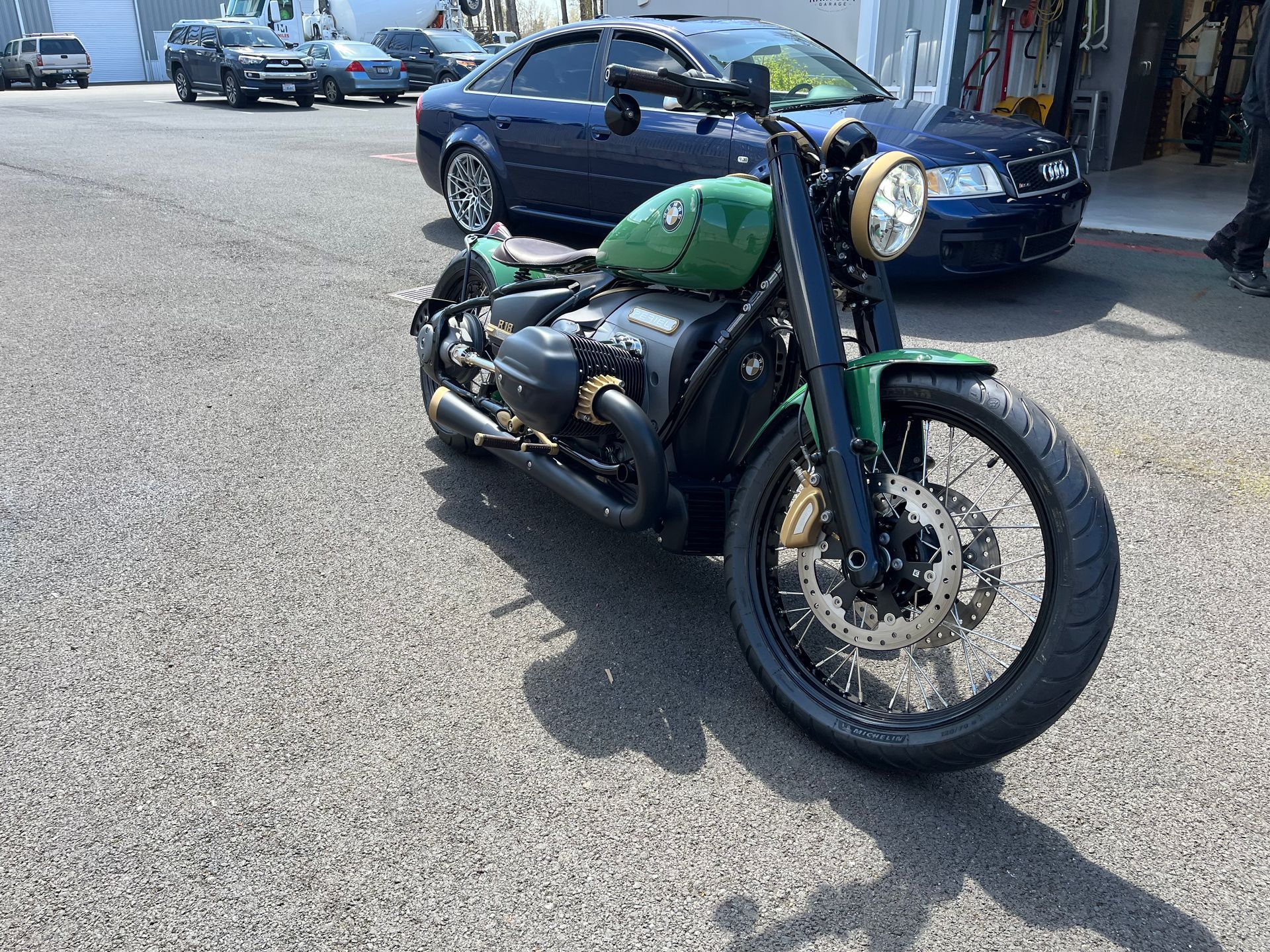 A green motorcycle is parked in a parking lot next to a blue car.
