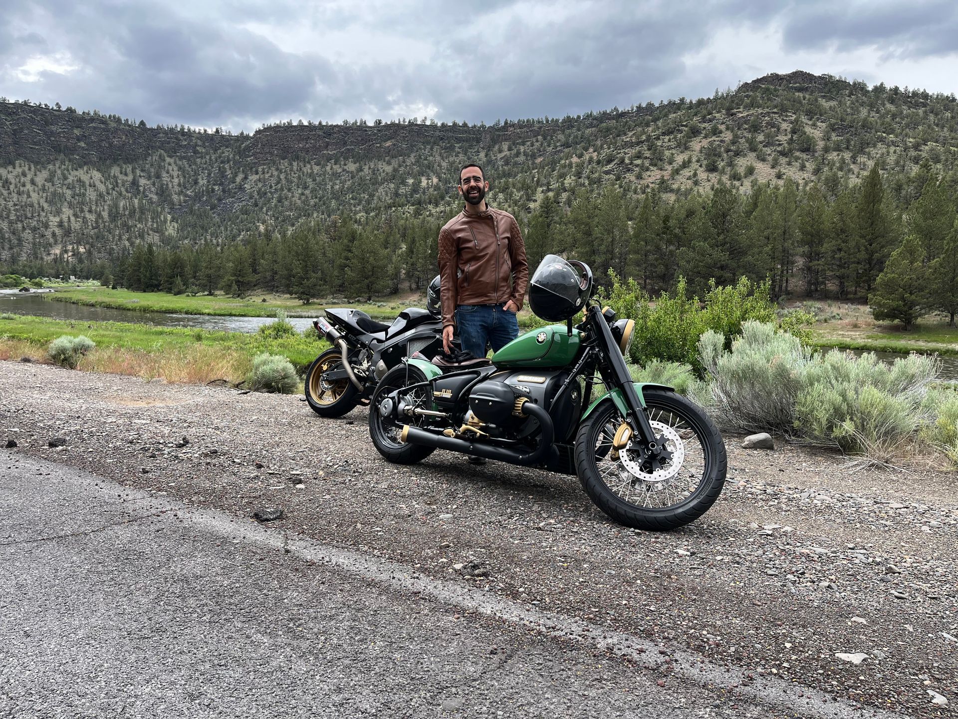 A man is standing next to a green motorcycle on the side of the road.