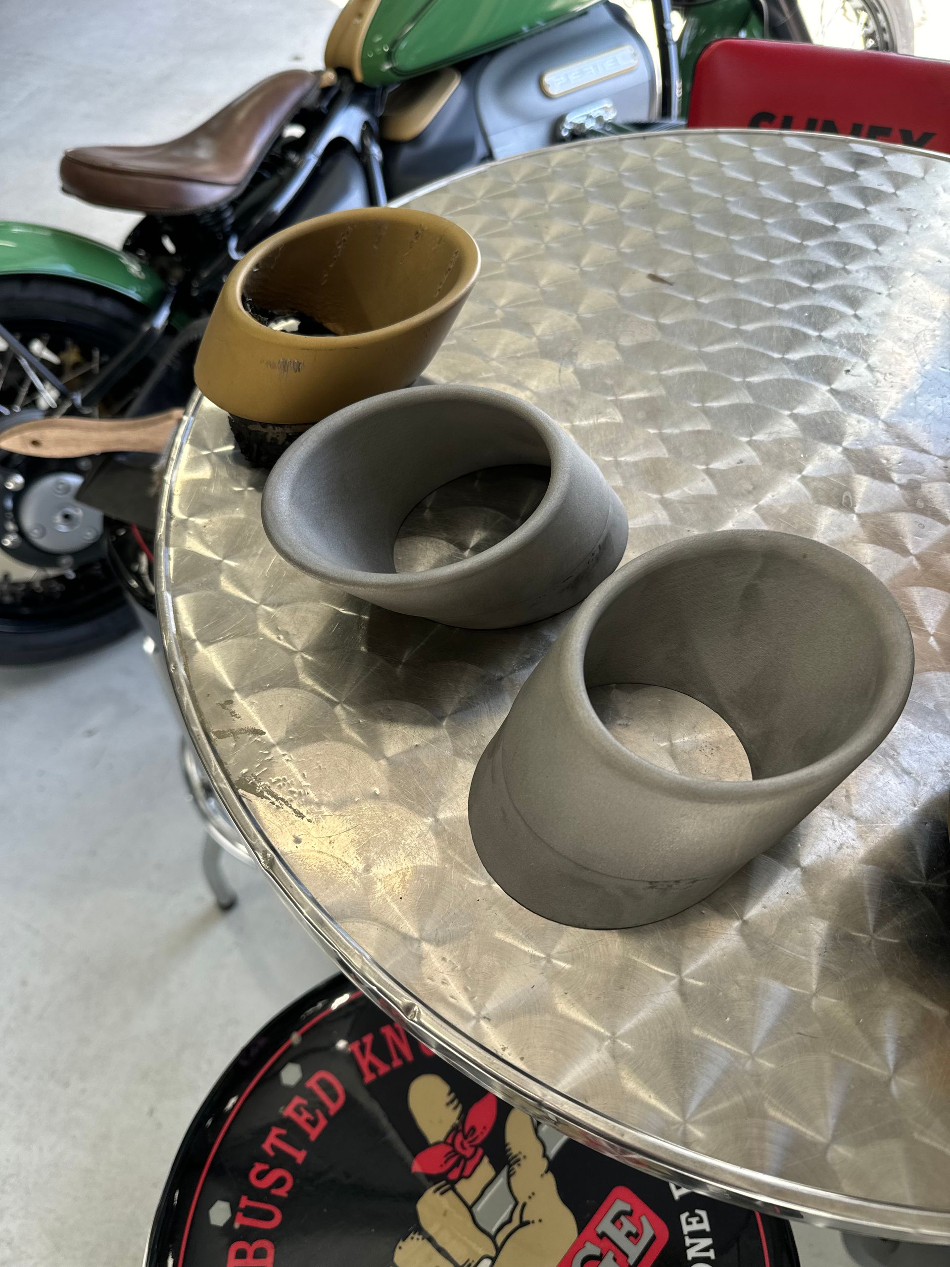 A motorcycle is parked in the background of a table with three cups on it