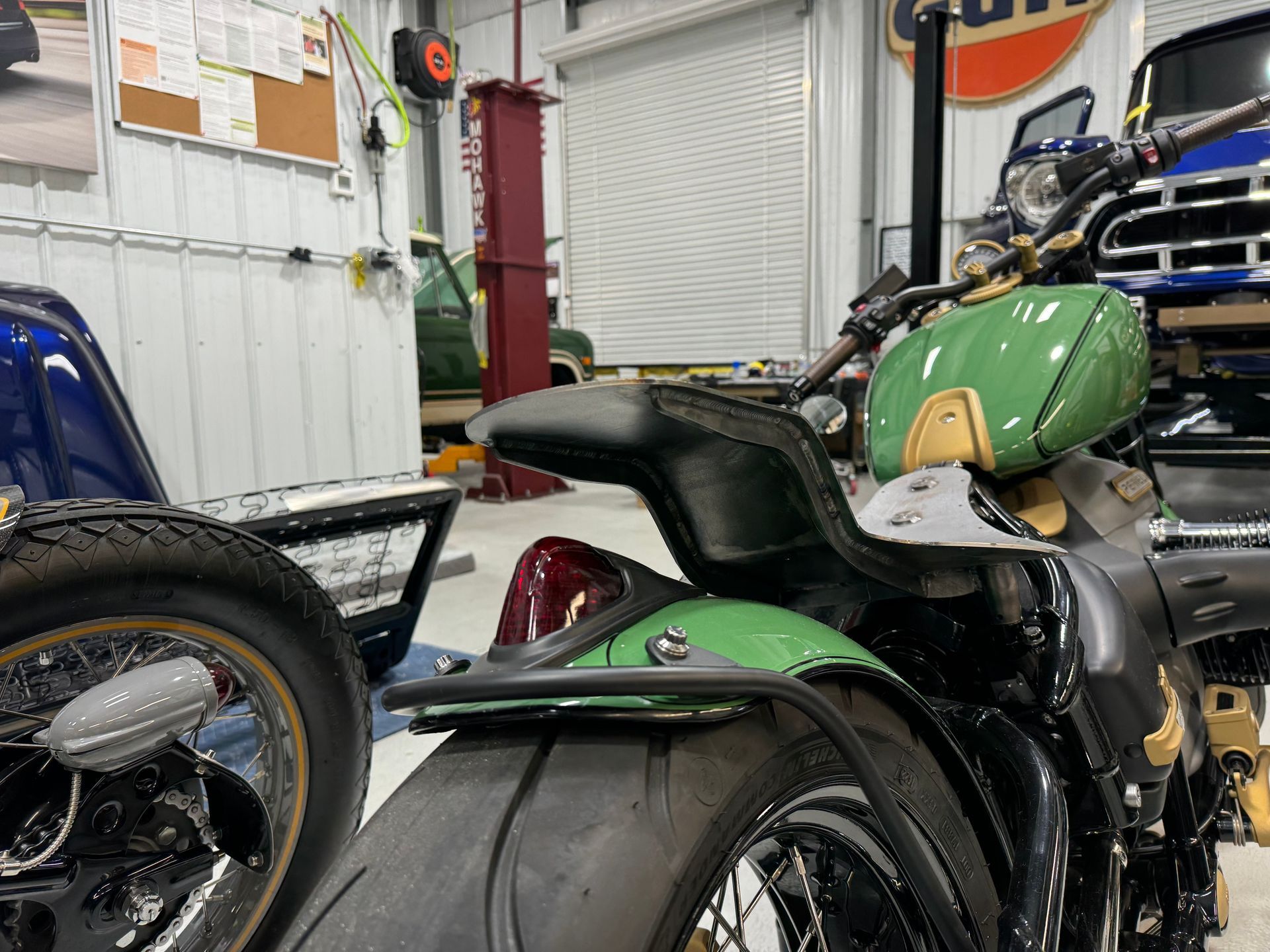 A green motorcycle is parked next to a black motorcycle in a garage.