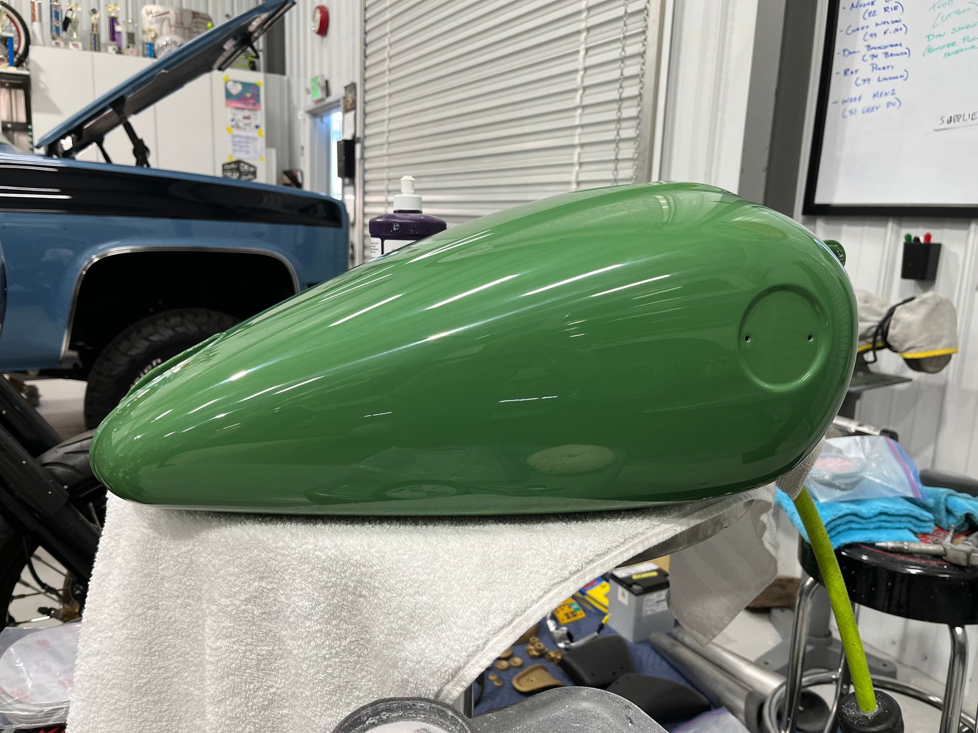 A green motorcycle gas tank is sitting on a towel in a garage.